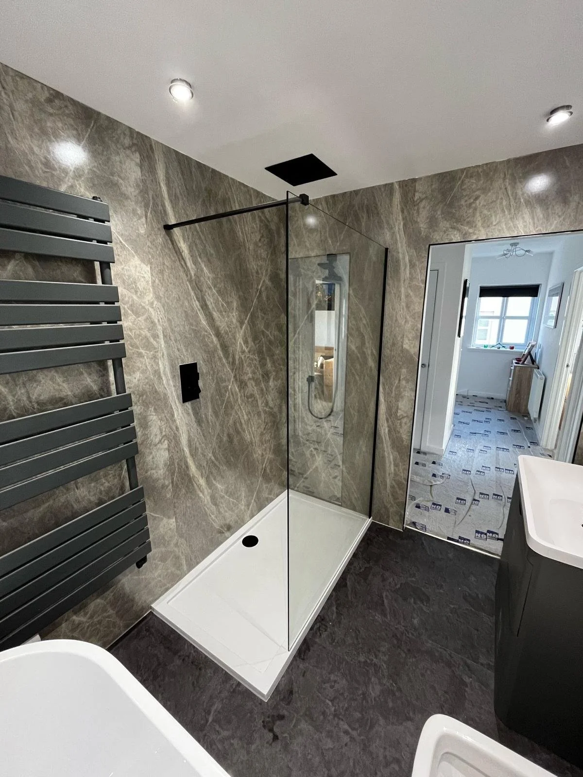 Modern bathroom with marble walls, walk-in shower with glass partition, black fixtures, and a gray towel radiator.
