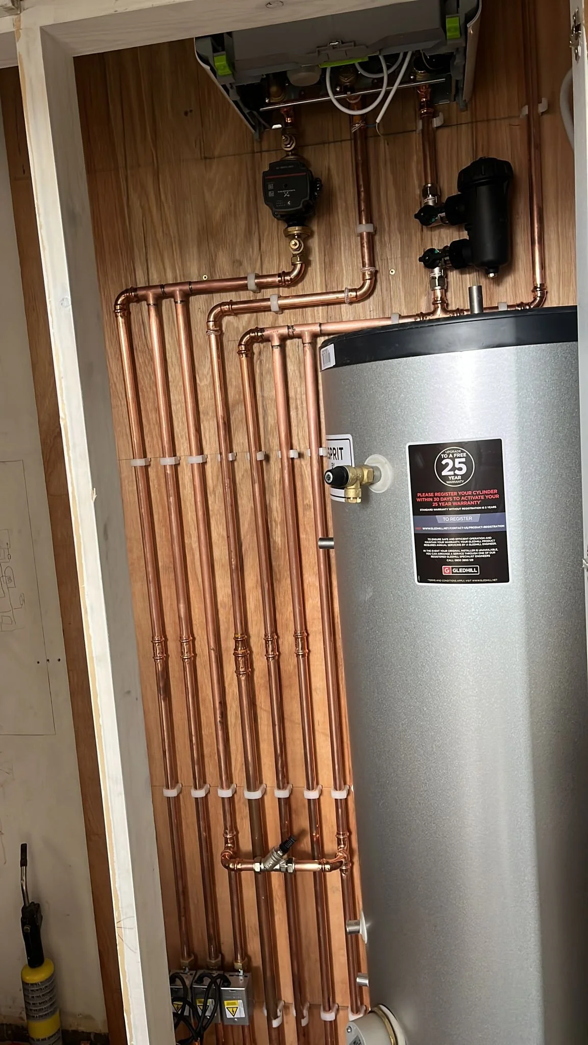 A water heater system with copper pipes, a pressure system, and control valves installed inside a wooden framed closet or utility space.