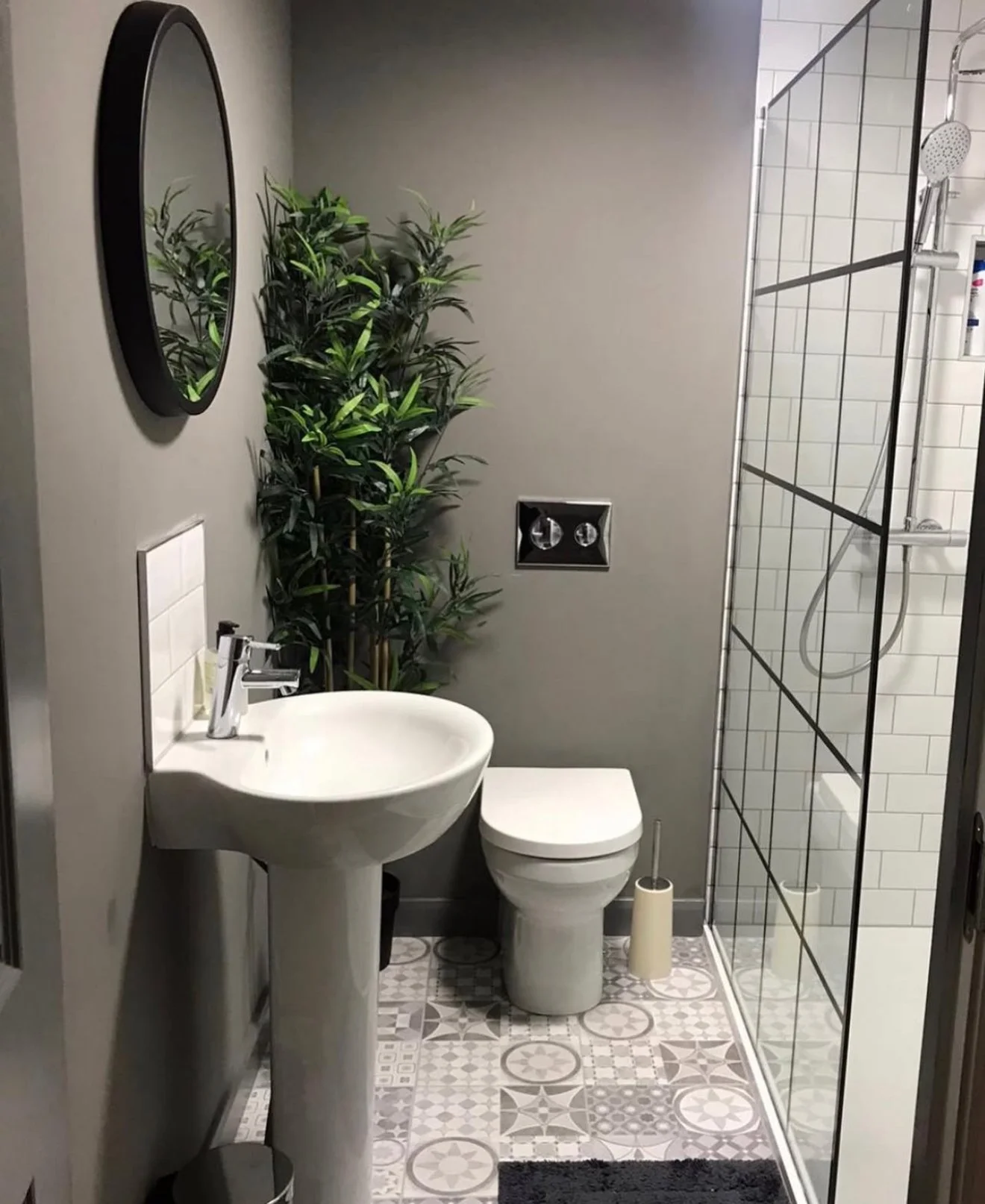 Small contemporary bathroom with gray walls, a pedestal sink, a toilet, a mirror, a tall green plant, and a glass-enclosed shower with white subway tiles.