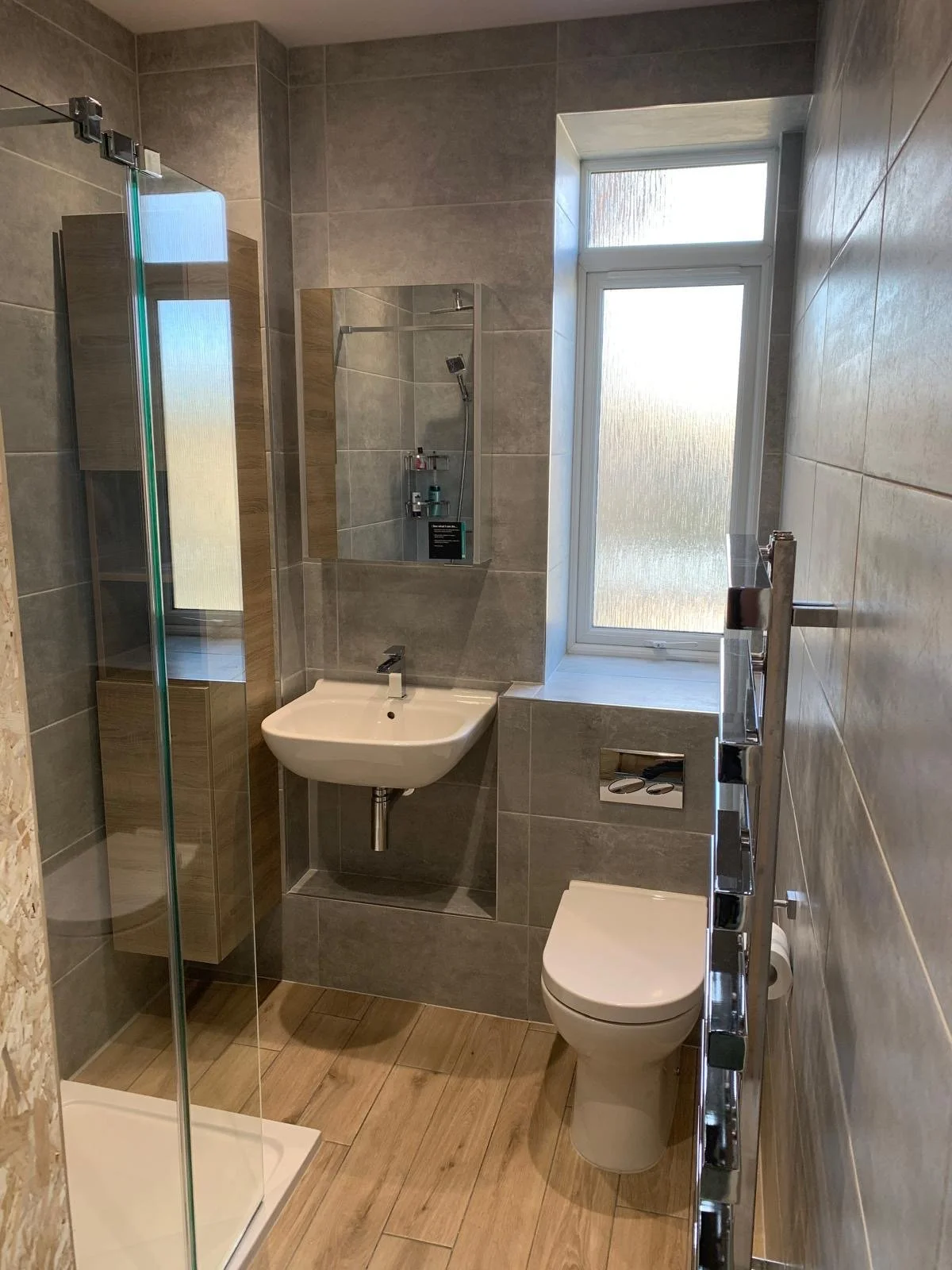 Small modern bathroom with shower, wall-mounted sink, toilet, and frosted window.