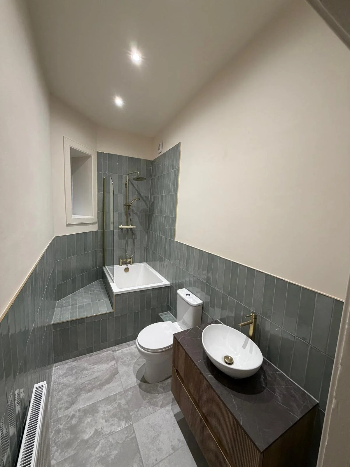 Modern bathroom with gray tiles, a white toilet, a wooden vanity with a vessel sink, and a shower with glass partition.