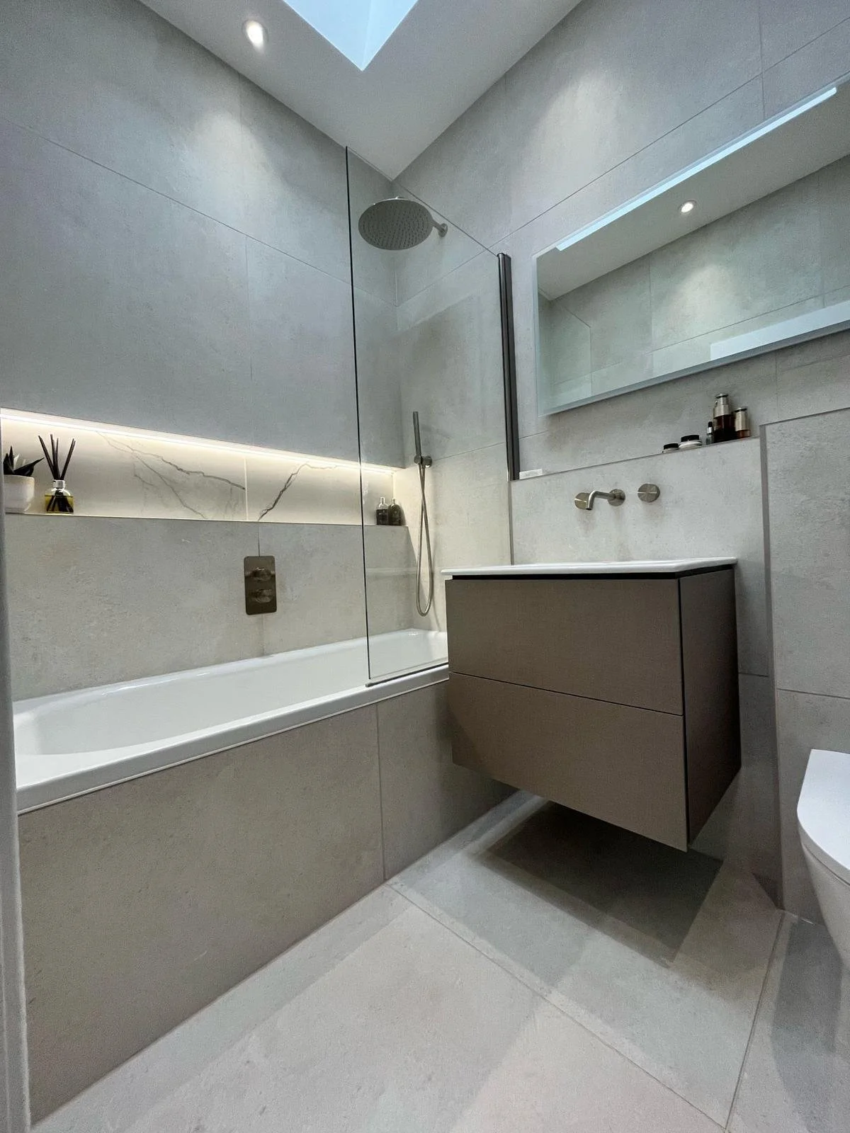 Modern bathroom with bathtub, glass shower partition, large mirror, gray floating vanity, and minimalist decor.
