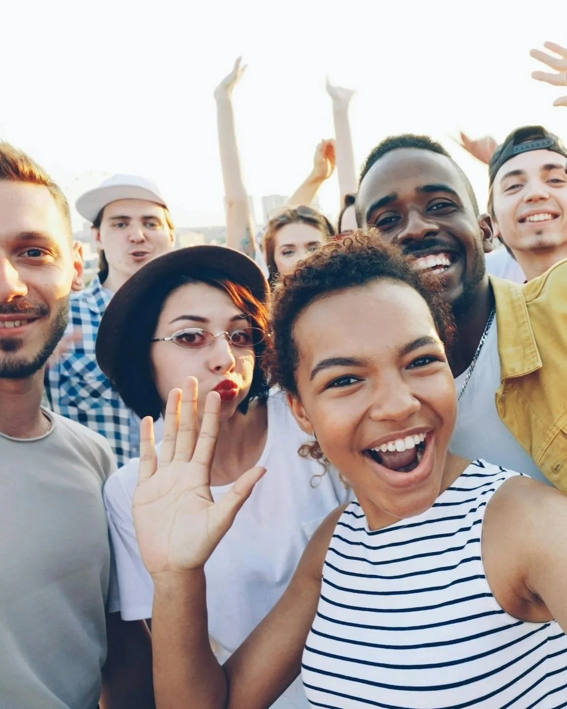 A diverse group of young people smiling and taking a selfie together outdoors.