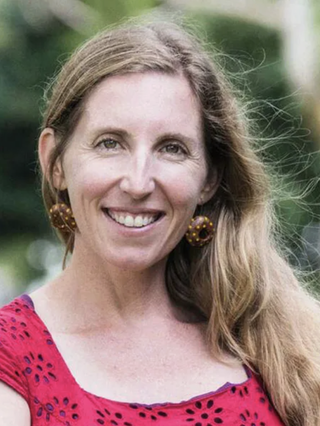 An image of a white woman with long blond hair and colourful circular earrings
