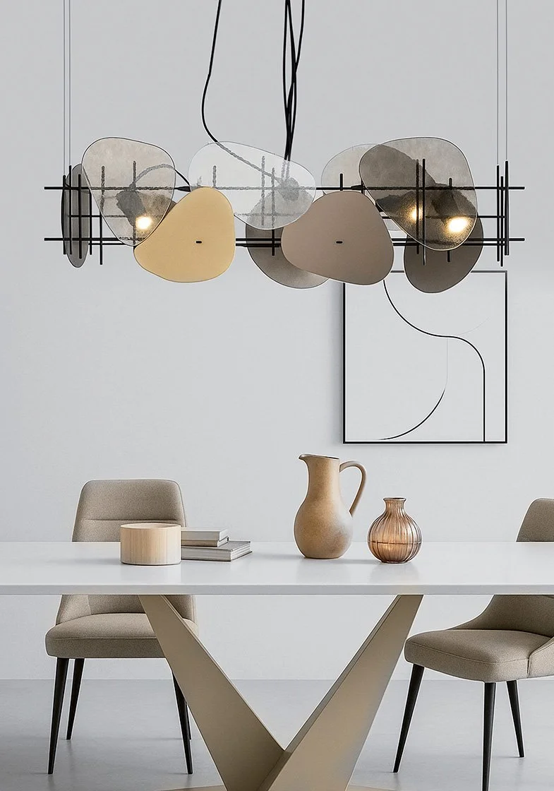 Mesa de jantar branca com duas cadeiras de estofado bege, decorada com três vasos (um grande, um médio e um pequeno). Há uma pintura abstrata com linhas pretas na parede e uma luminária moderna pendurada no teto com formas assimétricas em cores neutras.