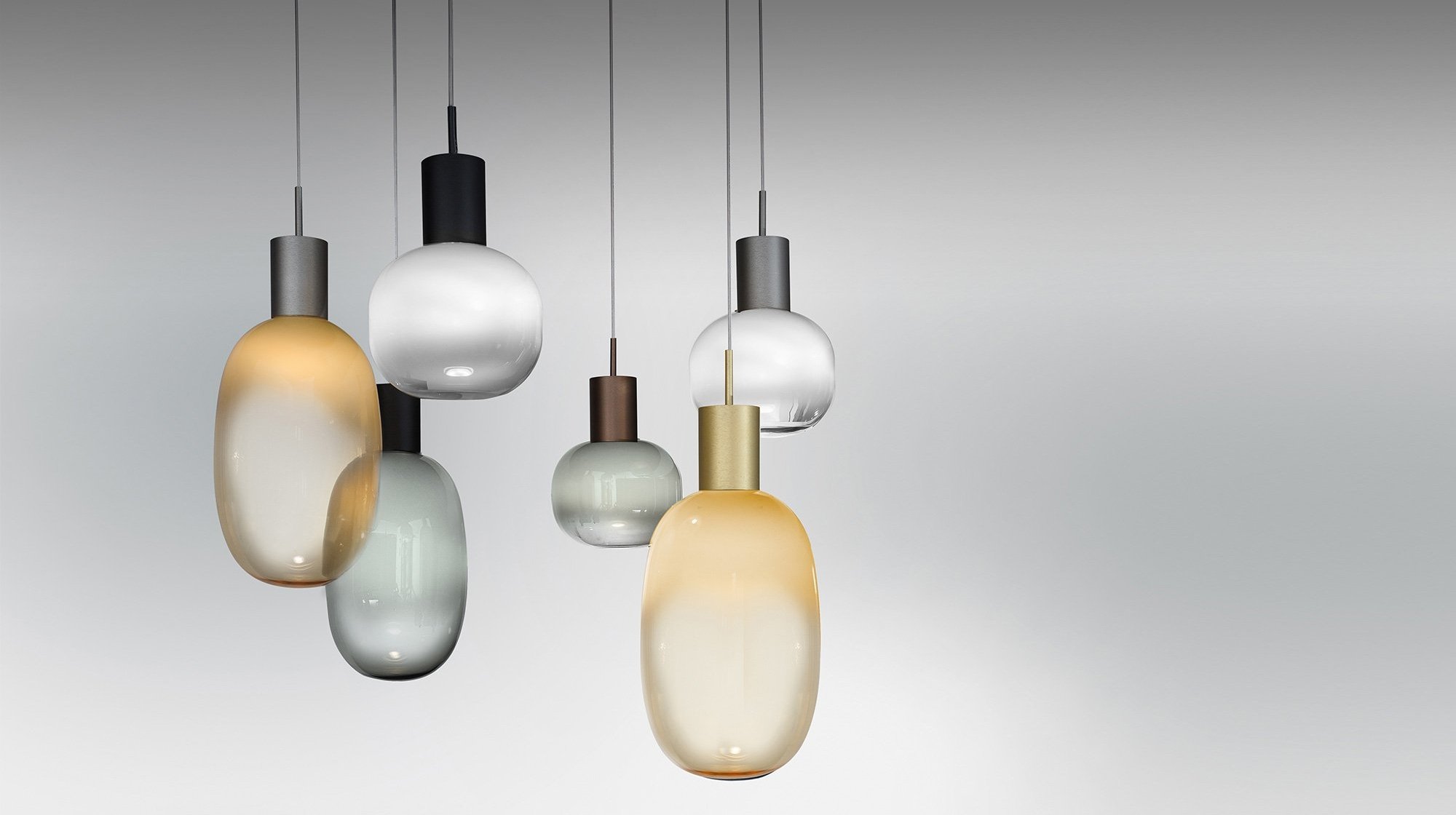 Lustres modernos com várias globos de vidro pendurados no teto, com diferentes tamanhos e cores suaves, em um fundo cinza claro.