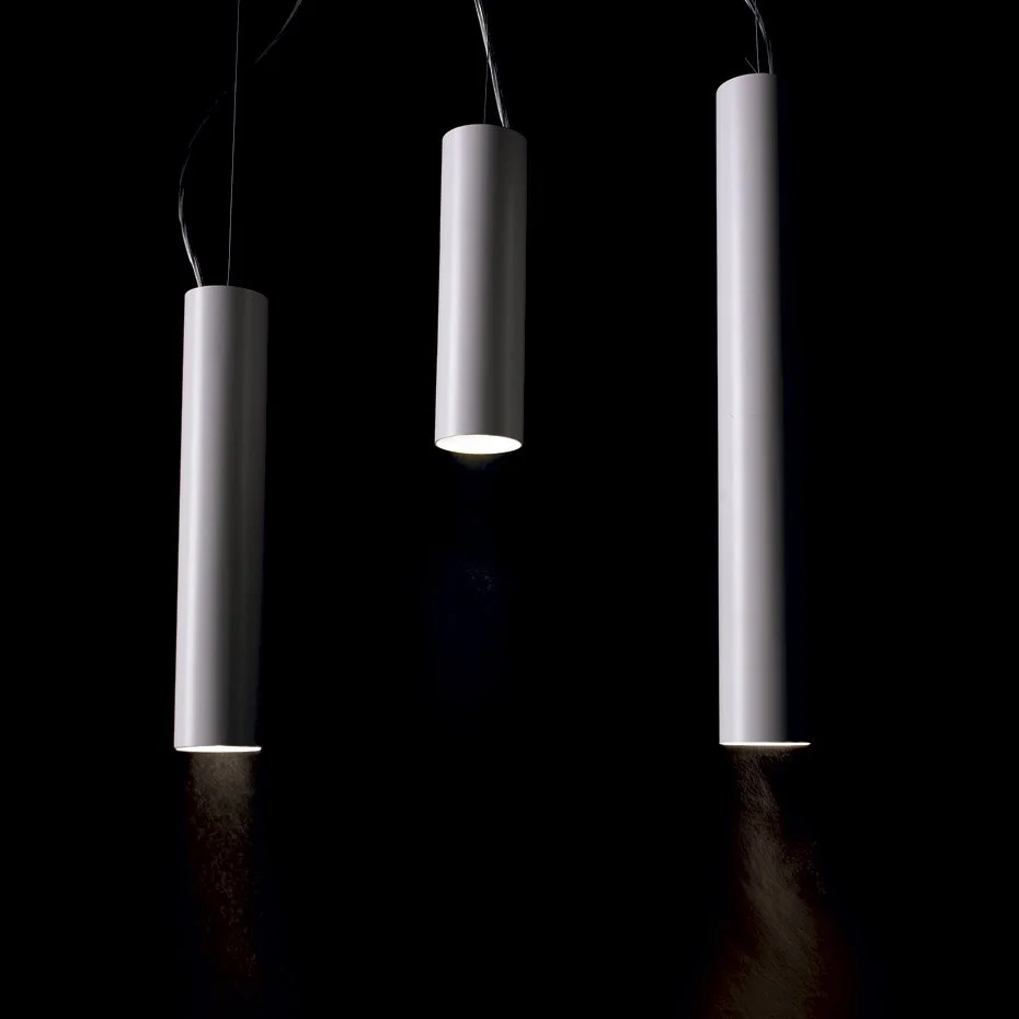Três luminárias penduradas em um teto escuro, de forma cilíndrica e branca, com luz direcionada para baixo.