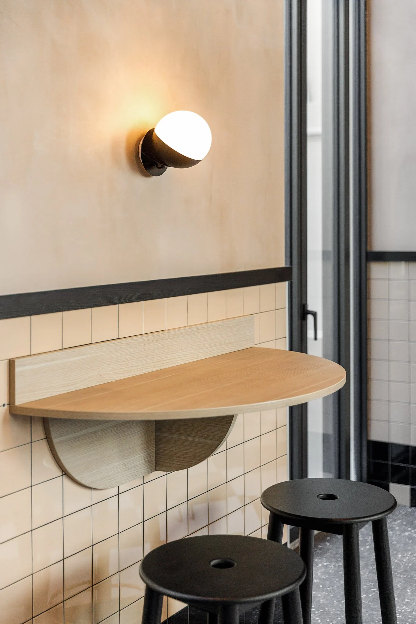 Ambiente decorado com bancada de madeira redonda, duas banquetas pretas e iluminação suave