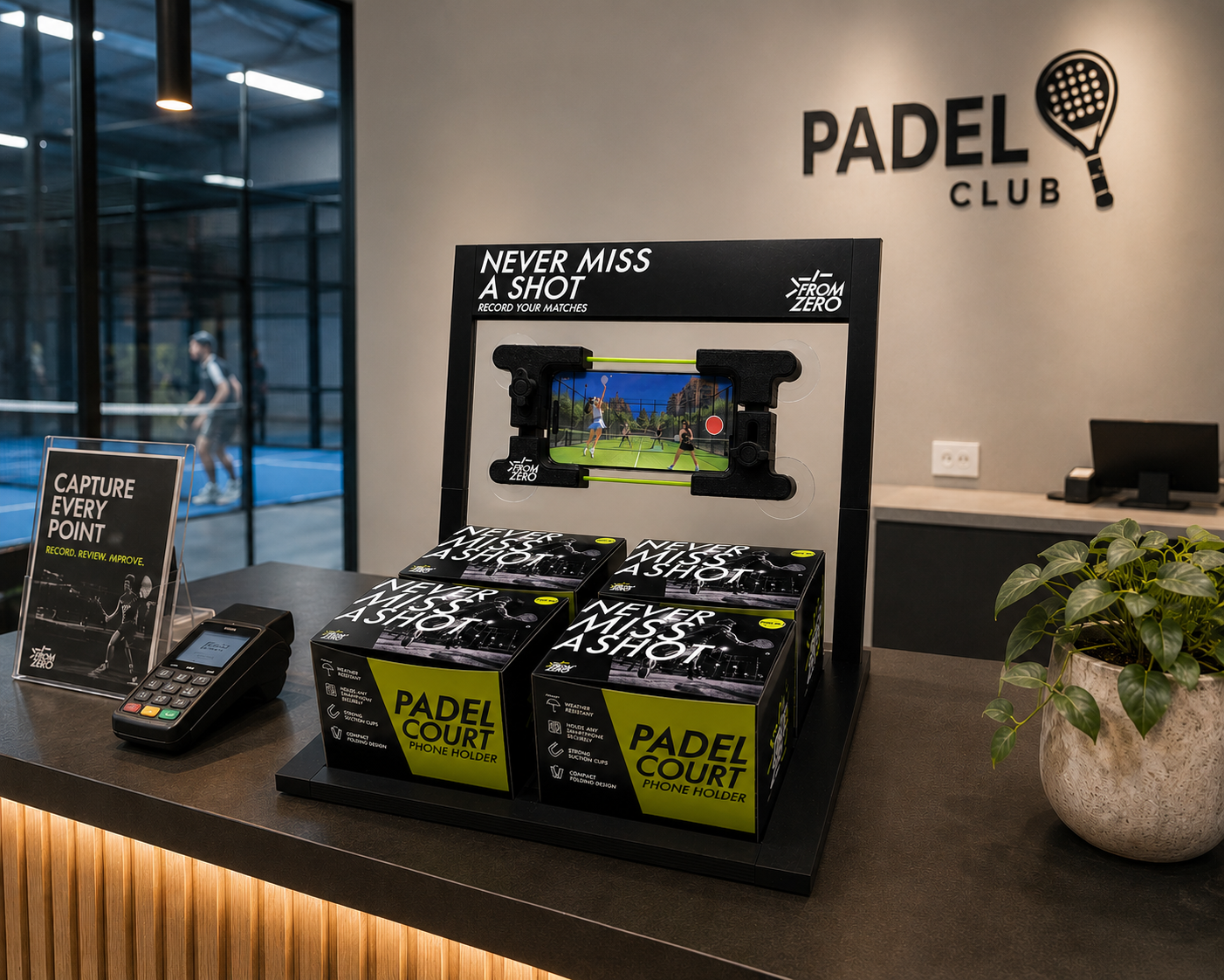 Padel club reception desk featuring a phone holder designed like a padel racket, promotional material titled 'Never Miss A Shot,' and a Point of Sale terminal with a sign encouraging capturing every point.