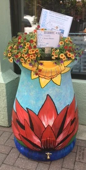 Colorful painted barrel with flowers and a certificate on top.