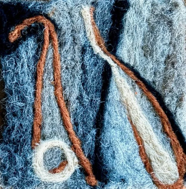 Close-up of a felted piece with brown and white yarns stitched on front.