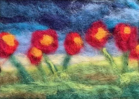 Felted artwork of red and yellow flowers with green stems and leaves against a blue sky background.