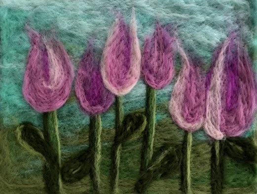 Felted wool artwork of pink tulips with green stems and leaves against a blue sky background.