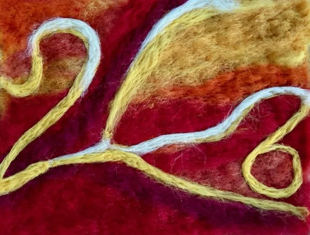 Close-up of felted piece in yellow and white on a red and orange background.