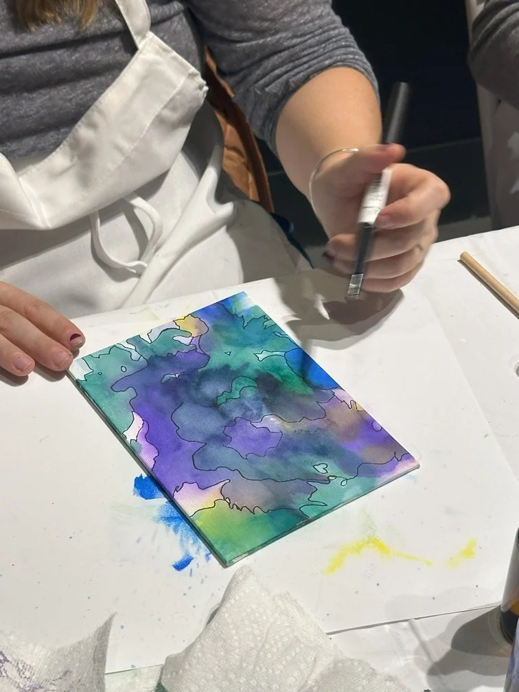 Person creating colorful abstract alcohol ink art on canvas panel.