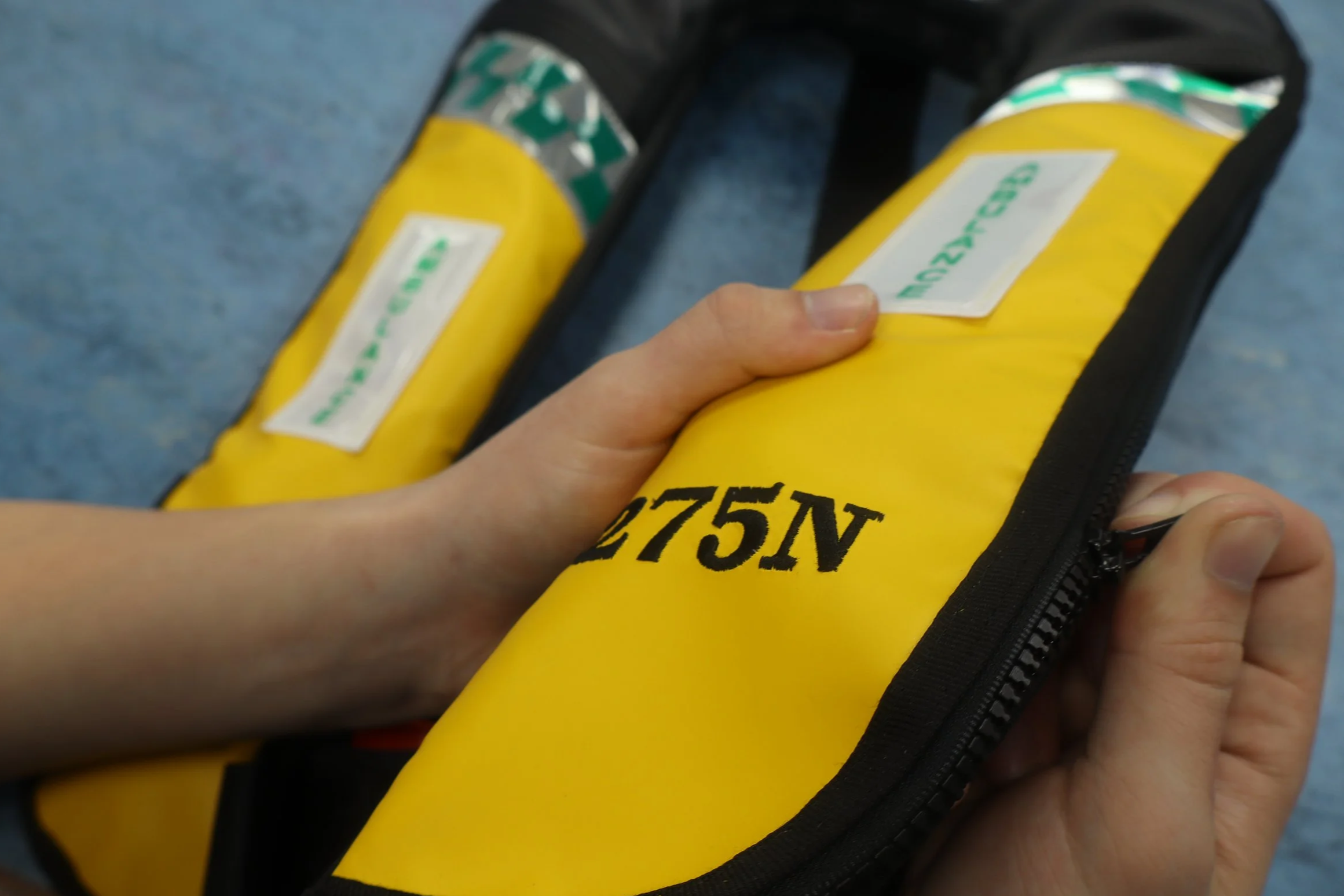 A hand holding a yellow lifejacket with a white label with green text.