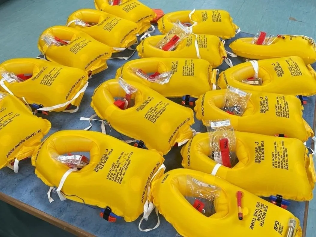 Multiple yellow life jackets with emergency tools, laid out on a blue surface.