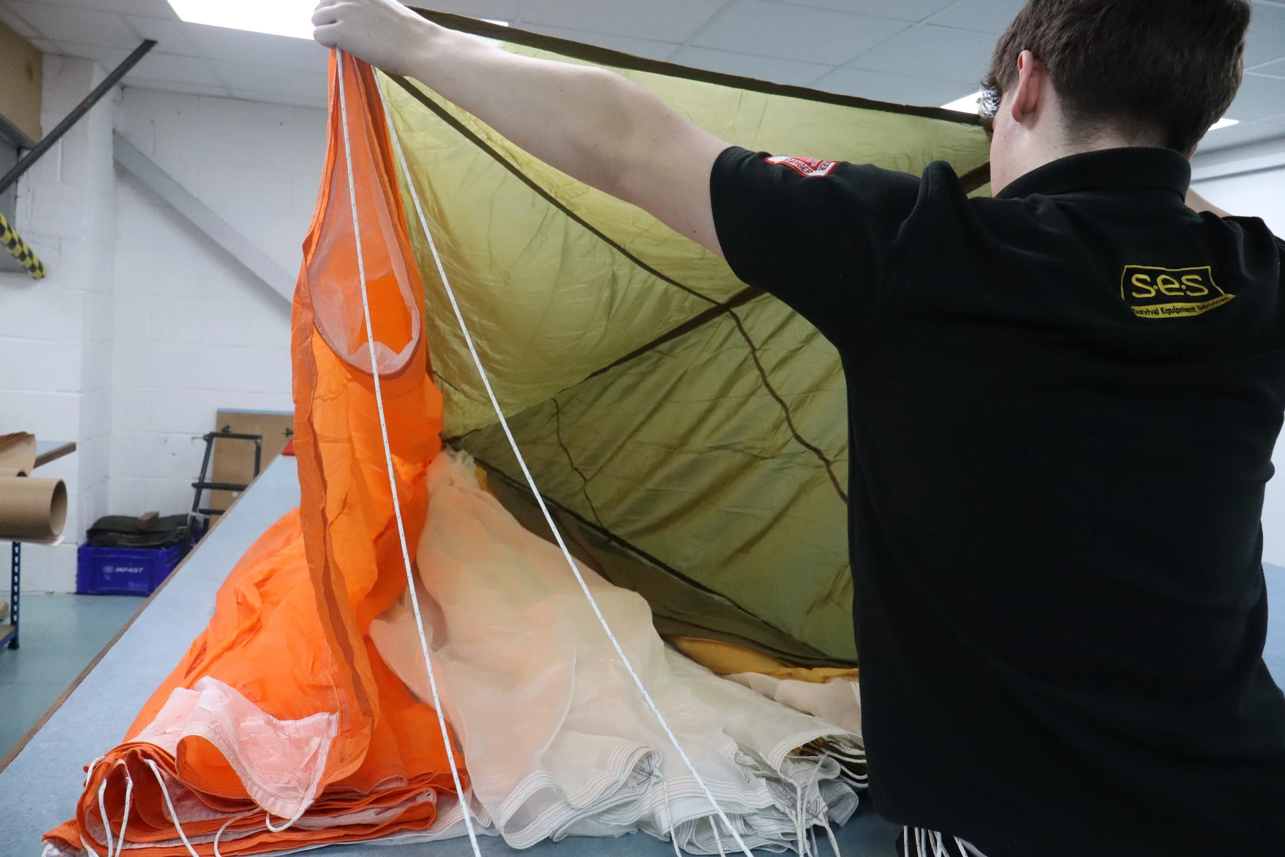 Person inspecting or preparing a rolled-up orange and beige parachute in a workshop.