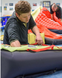 Two people working on large red and orange parachutes in an indoor setting.