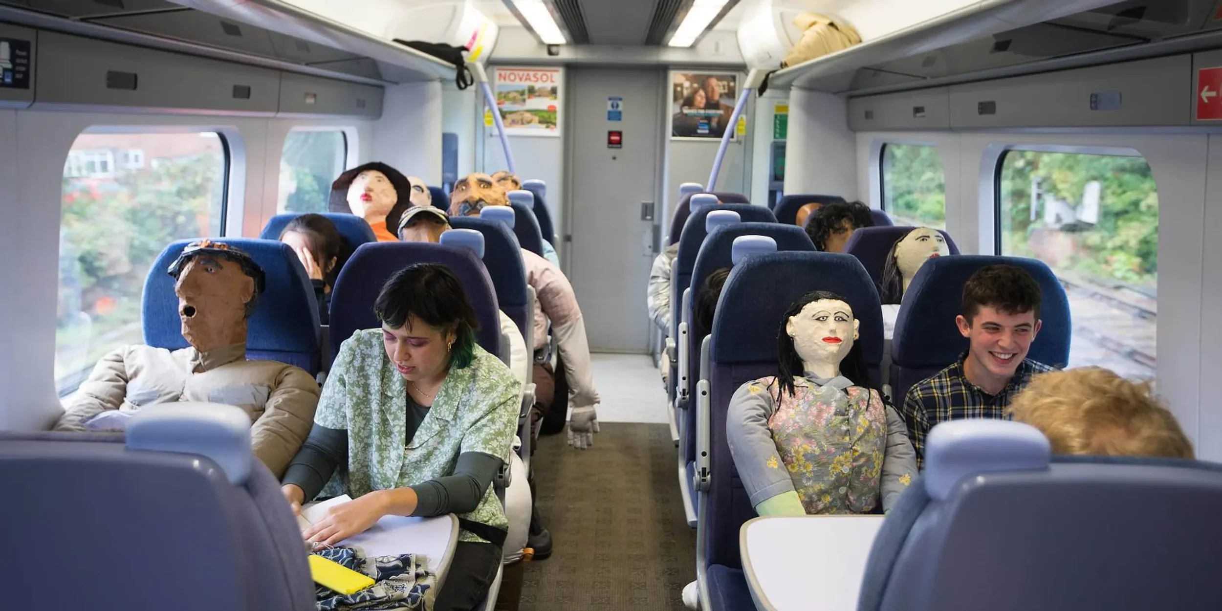 An art installation featuring people and handmade life-size dolls travelling in a train carriage.