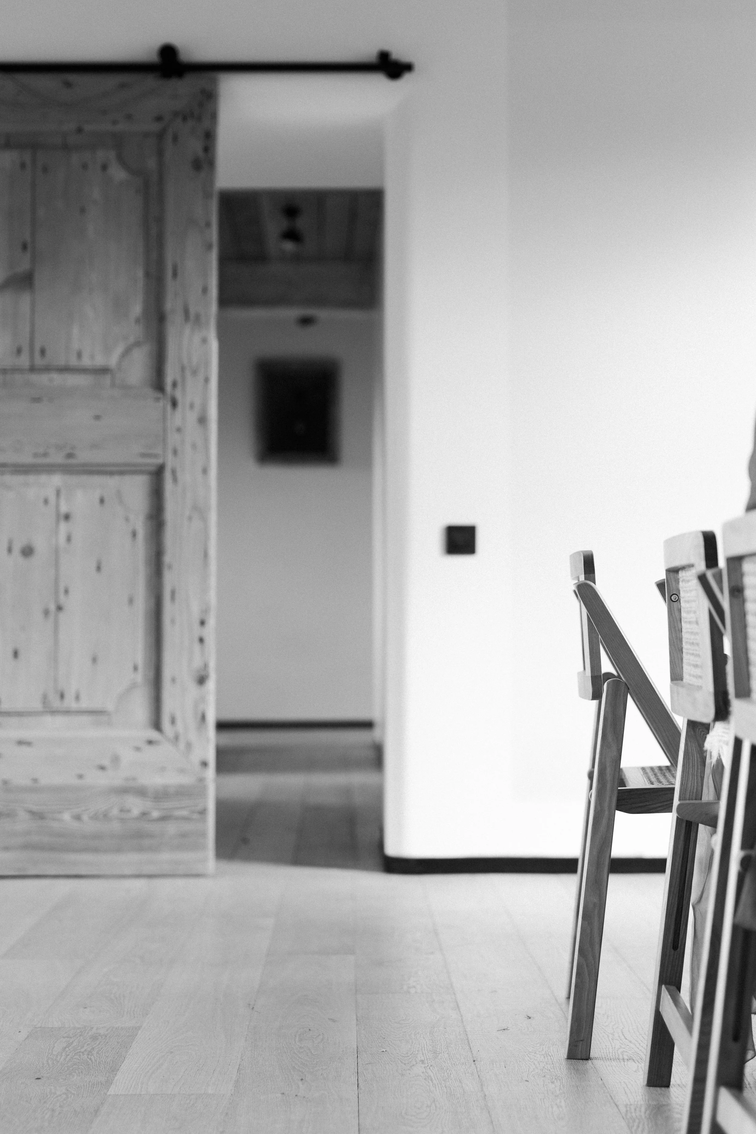 Une salle avec des chaises en bois alignées, un mur blanc et une porte en bois partiellement ouverte.