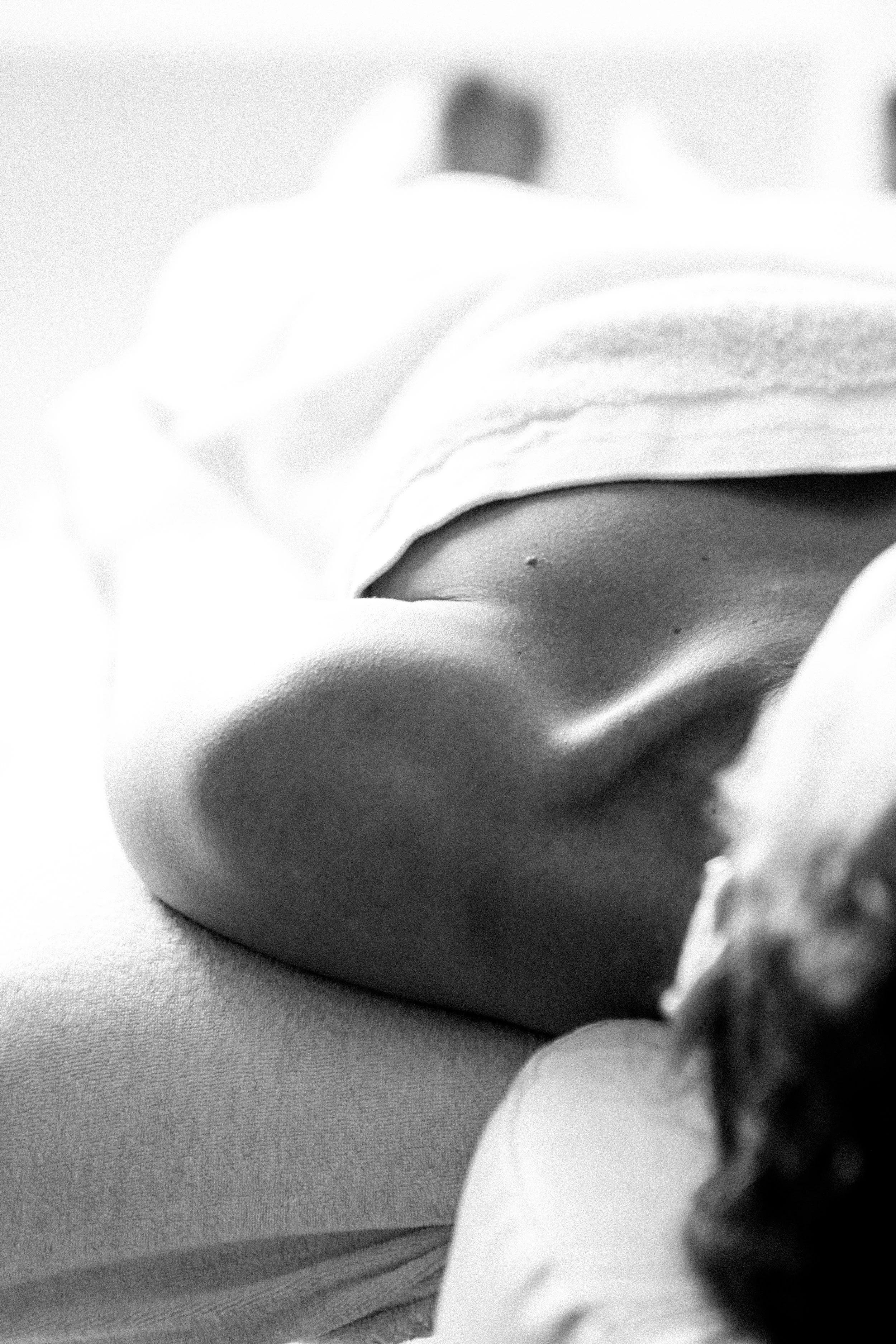 Photo en noir et blanc d'une personne allongée, vue de dos, avec un focus sur leur dos et leur épaule, portant un vêtement clair.