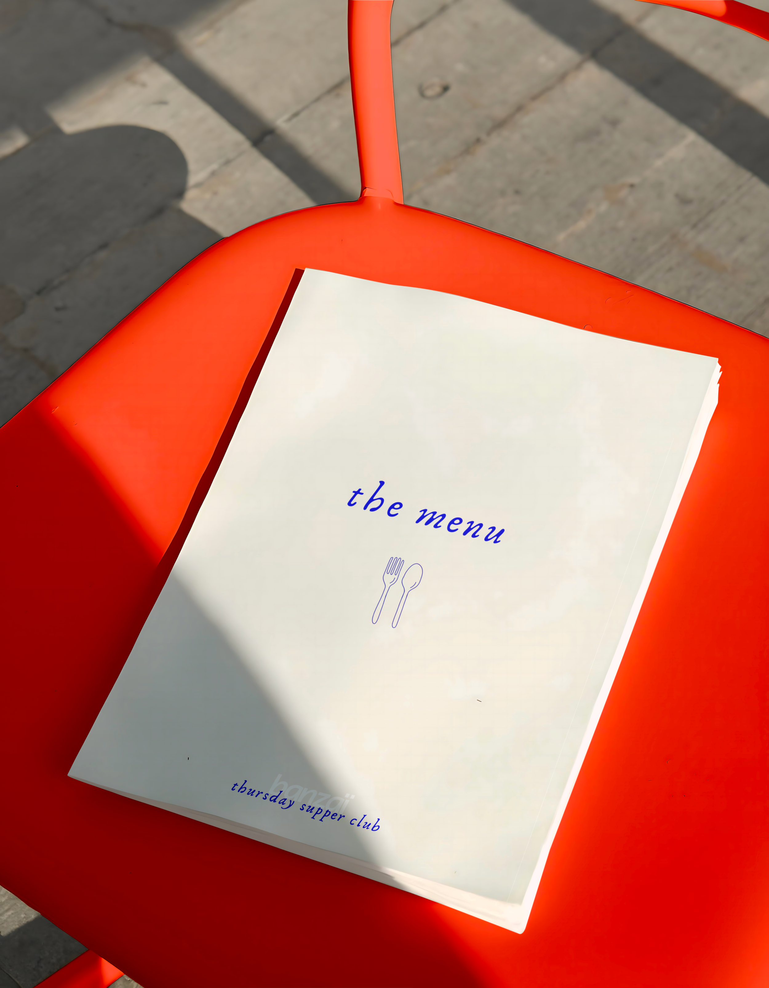 Un menu de restaurant posé sur une chaise rouge, avec un fond en pavés en extérieur.