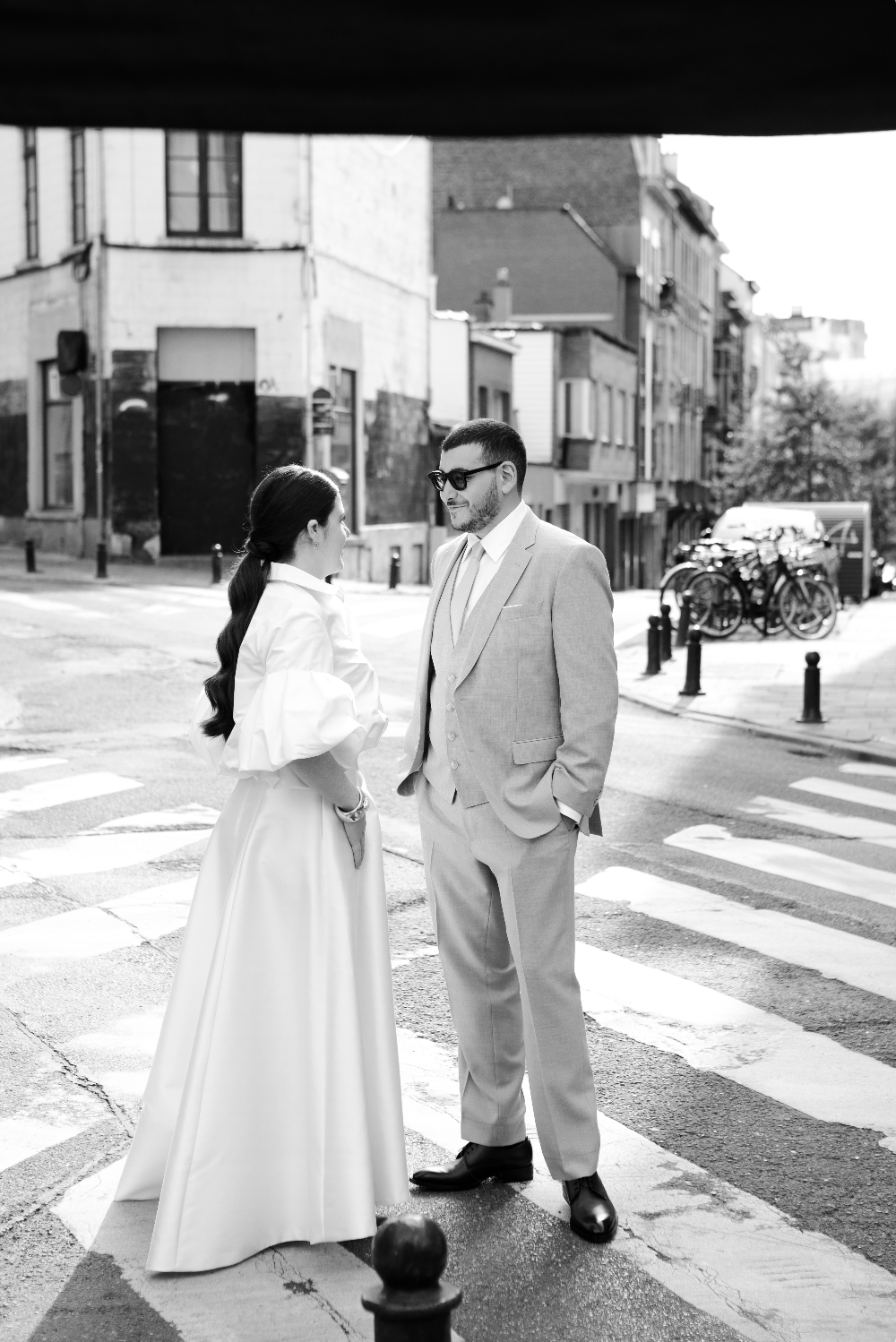 Un homme et une femme habillés élégamment se parlent dans une rue de ville, en noir et blanc.