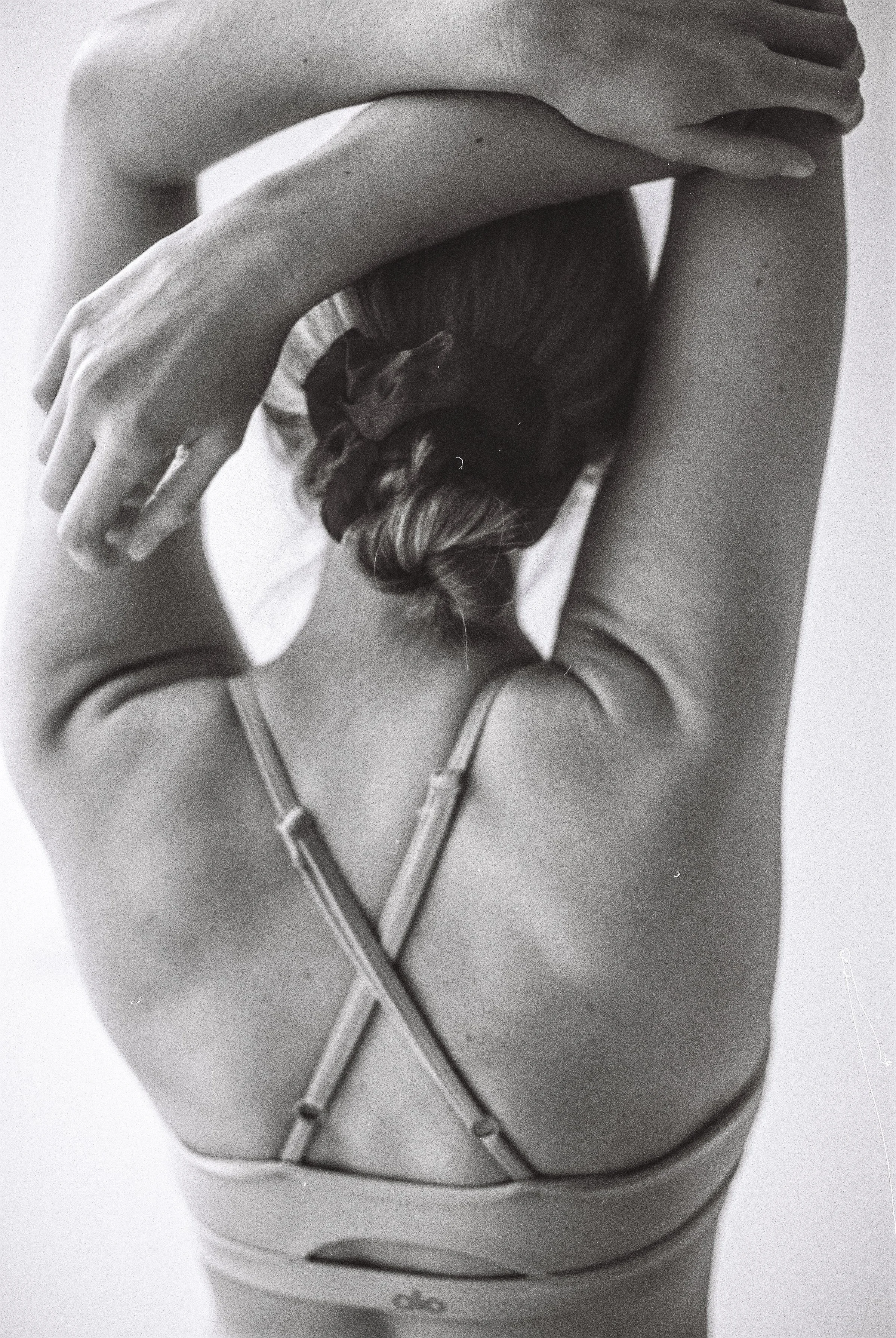 Une personne vue de dos, portant un débardeur à fines bretelles, avec un chat noir grimpé sur sa tête, dans une pose artistique en noir et blanc.