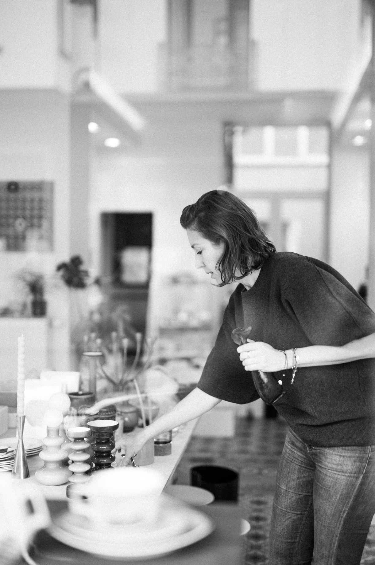 Femme regardant des objets decoratifs sur une table, en noir et blanc, intérieur moderne.