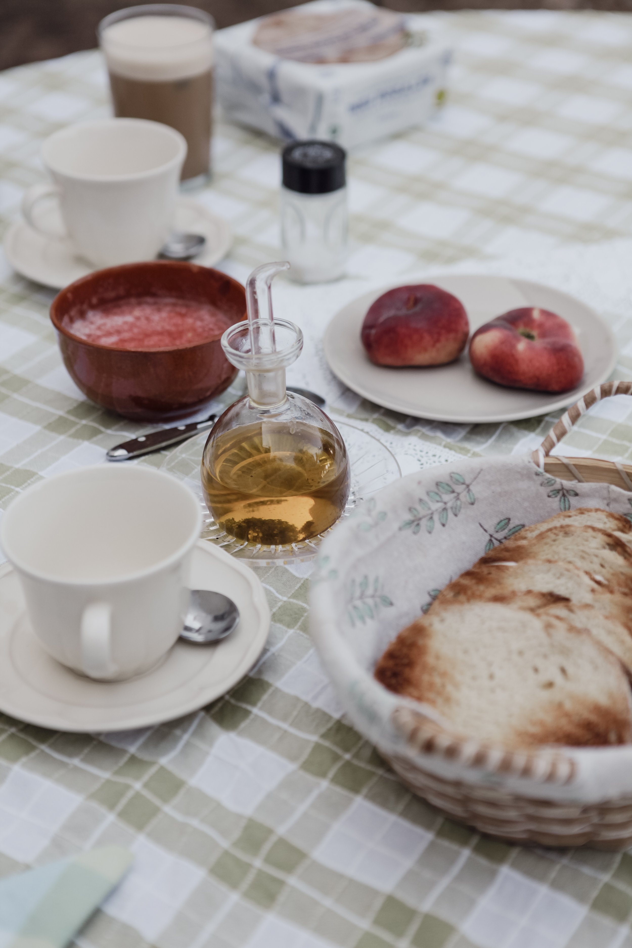 Petit déjeuner avec pain, pommes, thé, lait, sucre, miel, et un bol de soupe, sur une nappe à carreaux