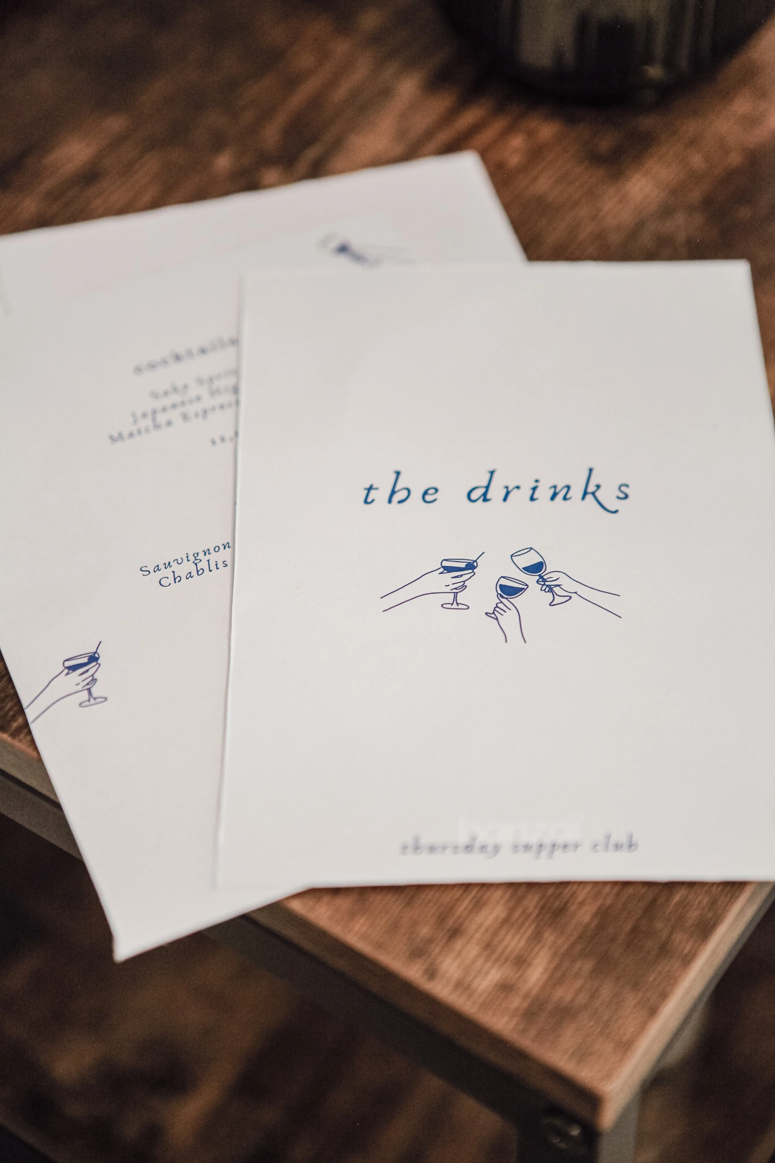 Menu avec le titre "the drinks" et une illustration de quatre mains tenant des verres à vin ou à cocktail.