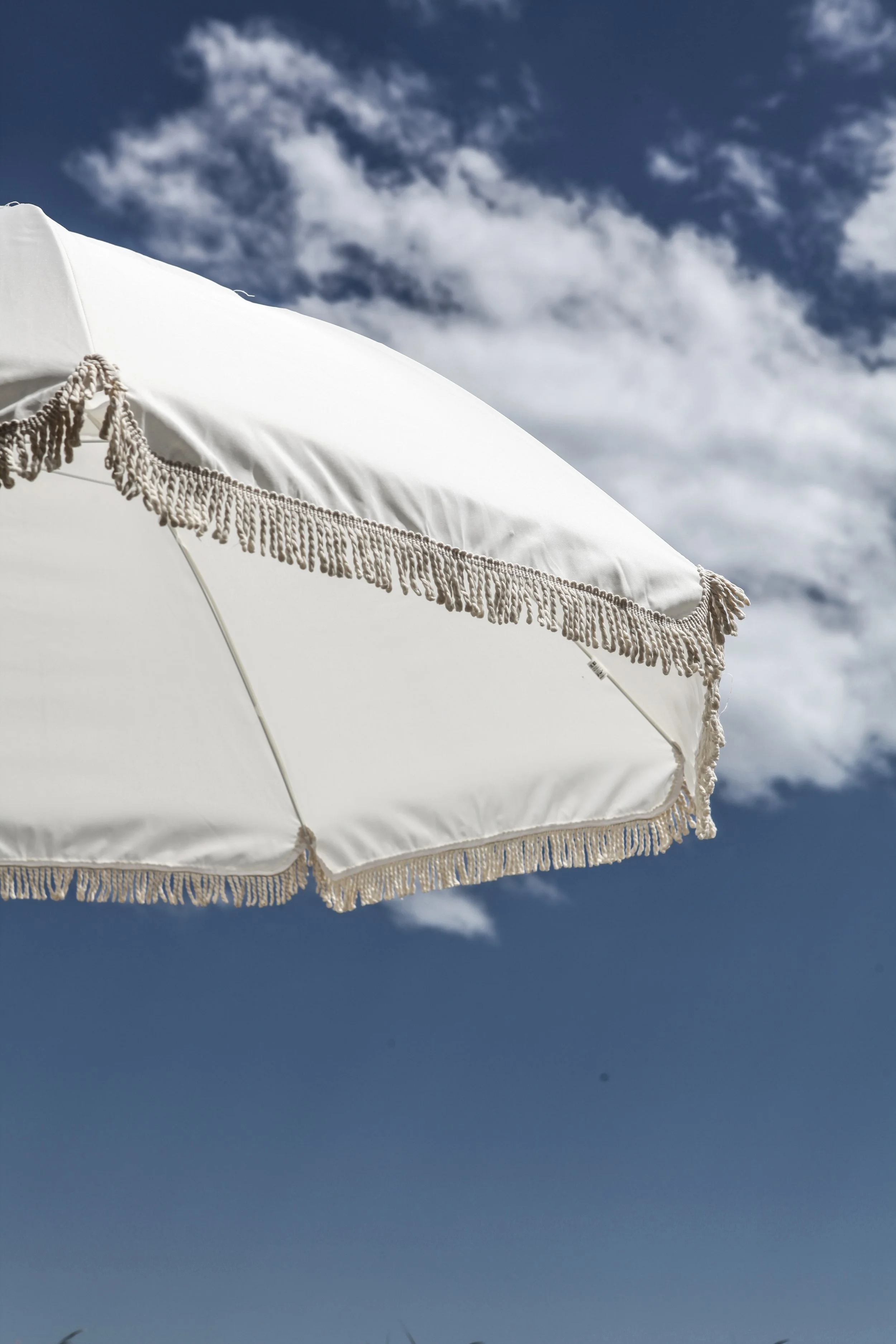Un parasol blanc avec des franges suspendues, sous un ciel partiellement nuageux.