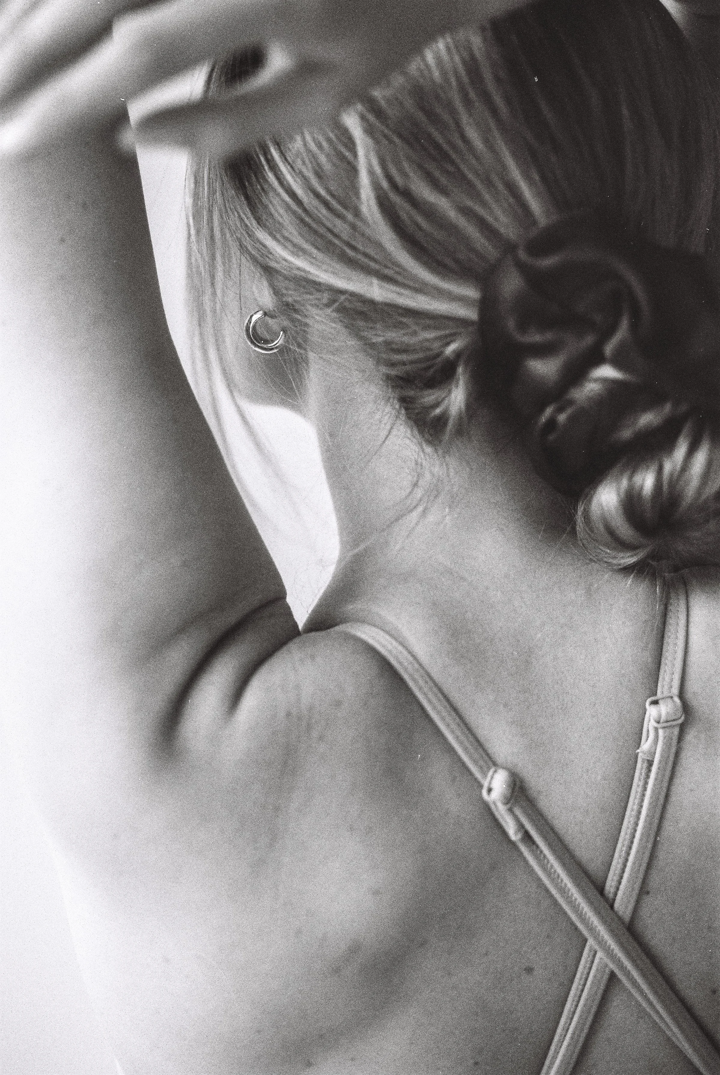 Une femme vue de dos, avec des cheveux attachés en chignon, portant un haut à baillettes et une veste en coton, dans un style artistique en noir et blanc.