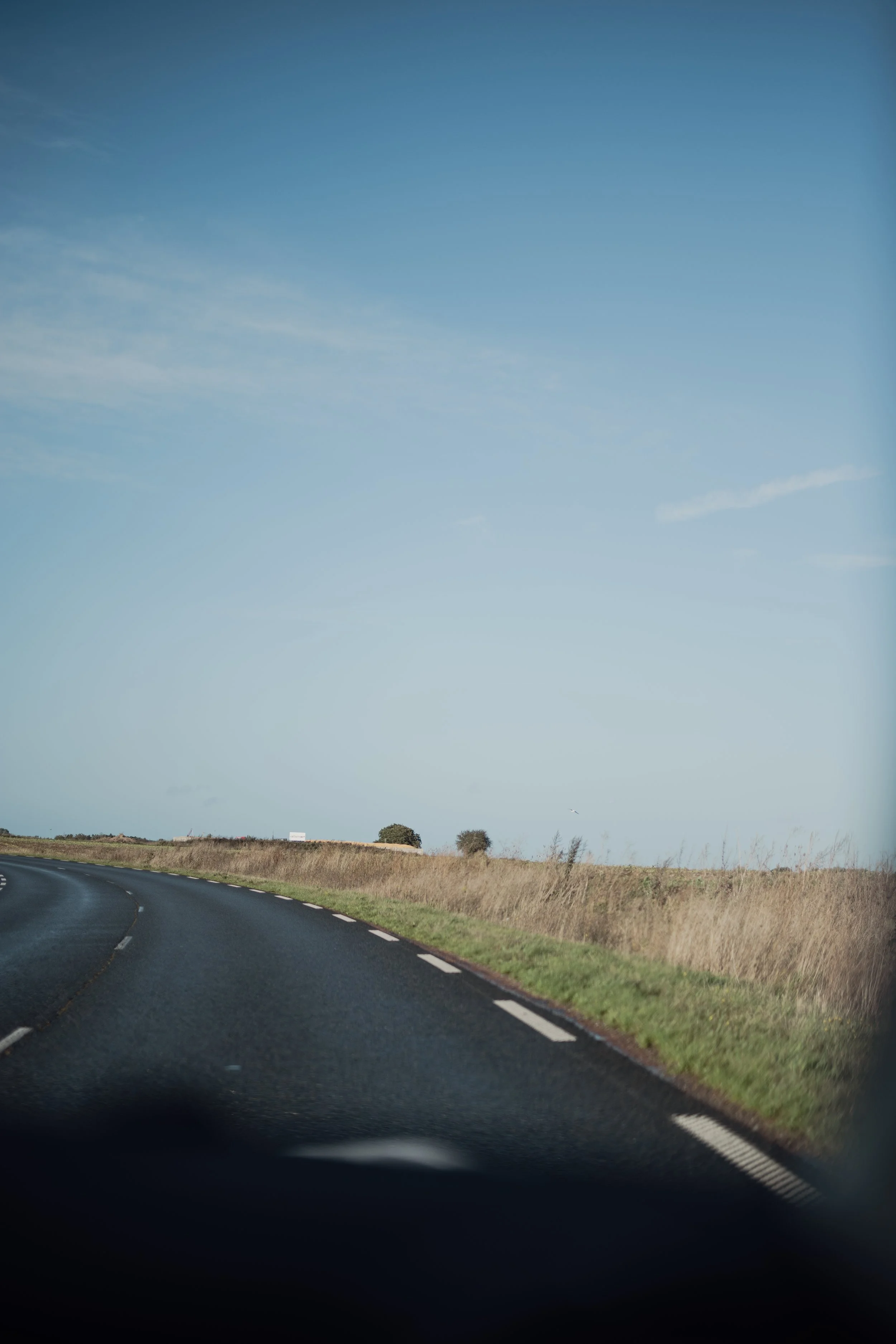 Une route sinueuse traversant un paysage rural avec un ciel clair et quelques arbres en arrière-plan.