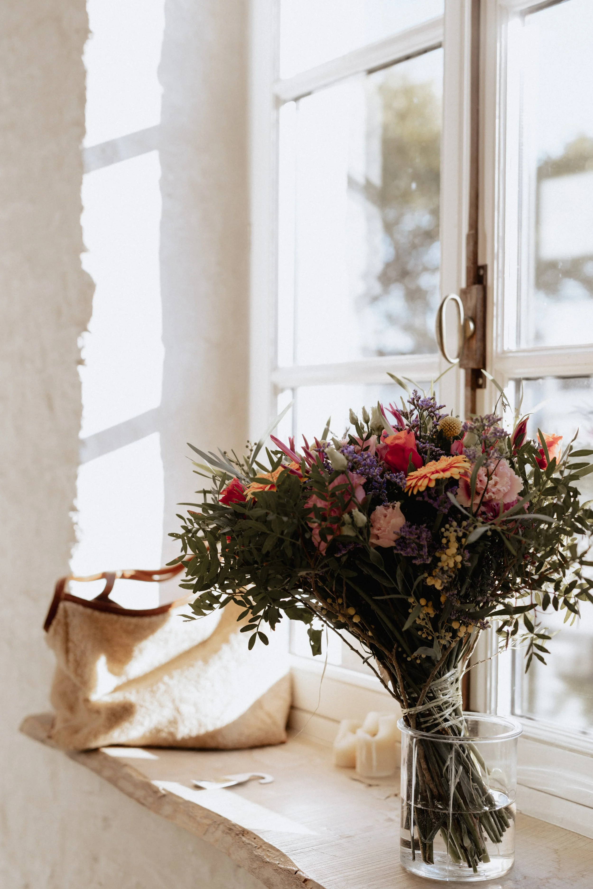 Un bouquet de fleurs colorées dans un vase en verre sur une fenêtre avec une vue extérieure floue.