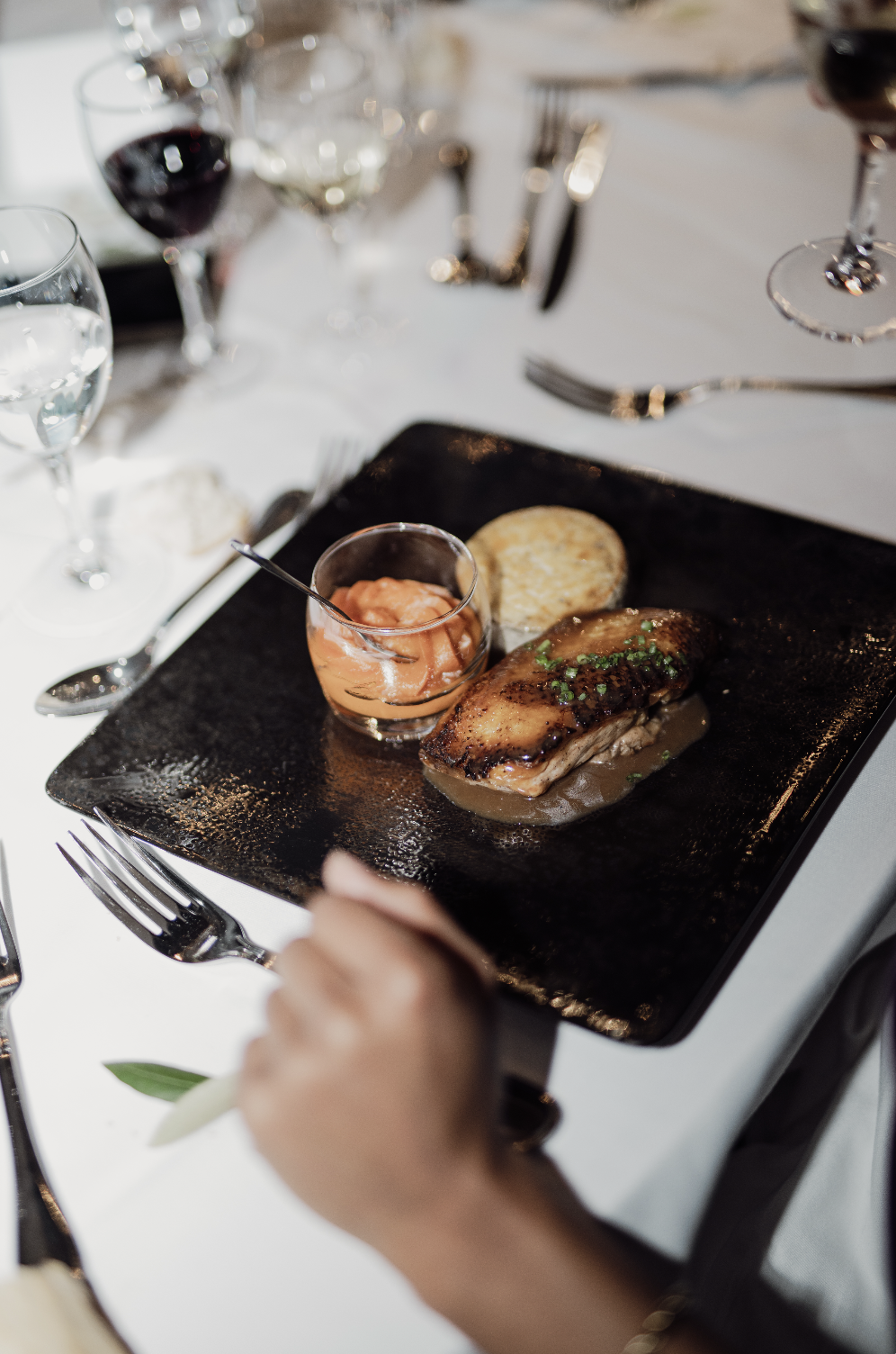 Assiette avec un filet de poisson avec sauce, accompagnée de pommes de terre rôties et d'une sauce rosée, dans un cadre élégant.