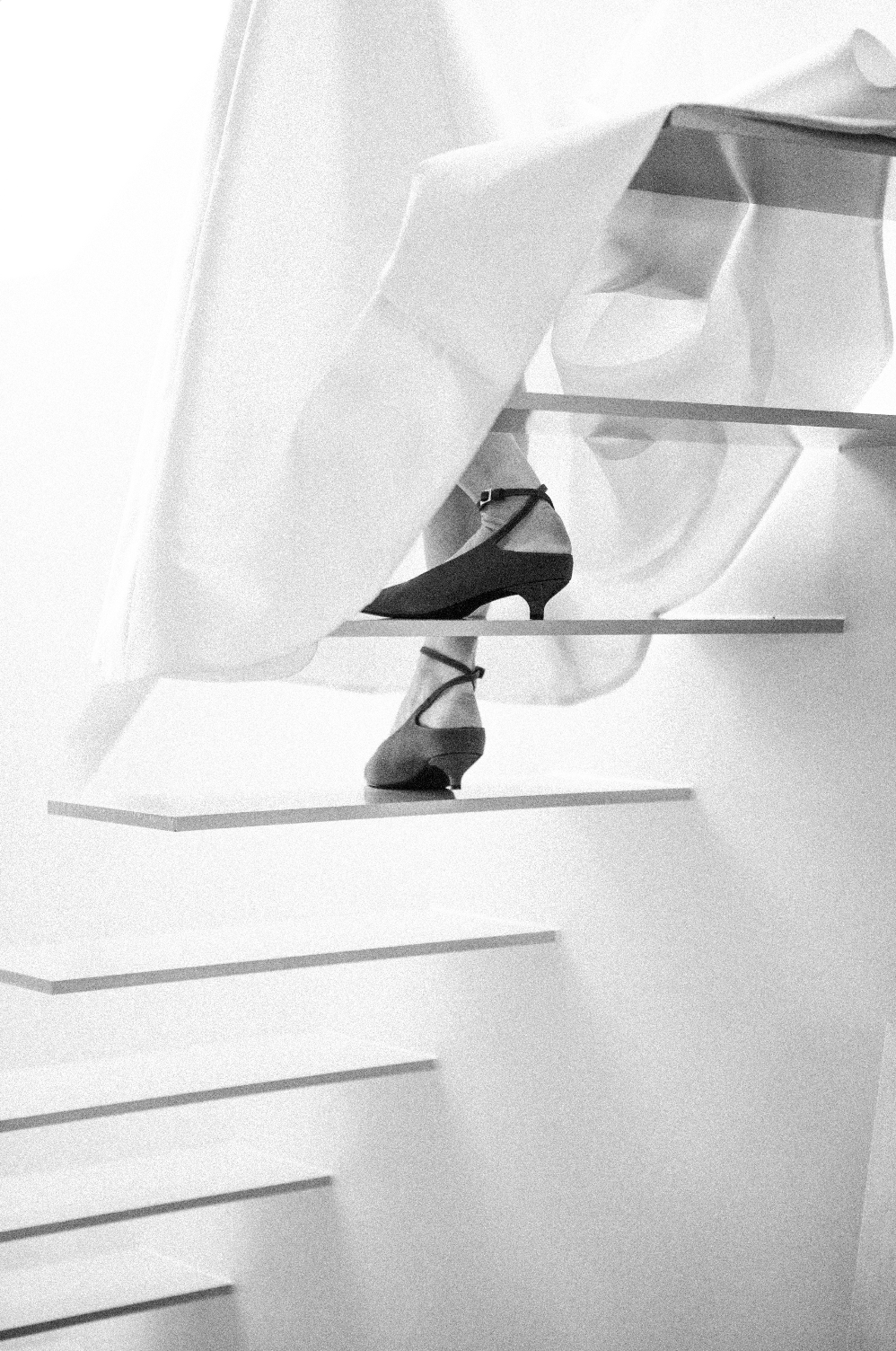 Une paire de chaussures à talons noirs exposée sur des étagères dans une vitrine, en noir et blanc.