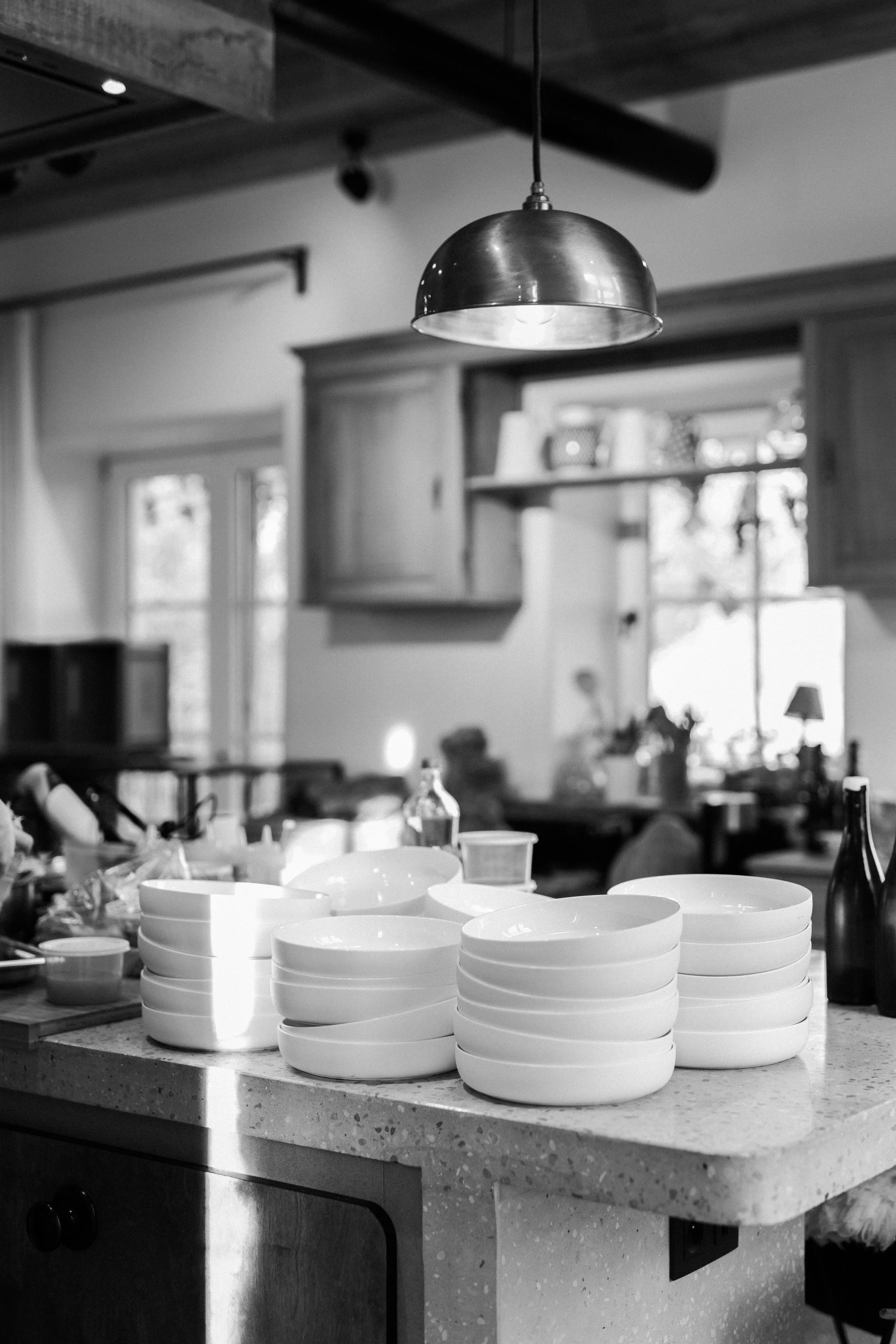 Assiettes blanches empilées sur un plan de travail de cuisine, éclairé par une lampe suspendue en métal, dans une cuisine intérieure.