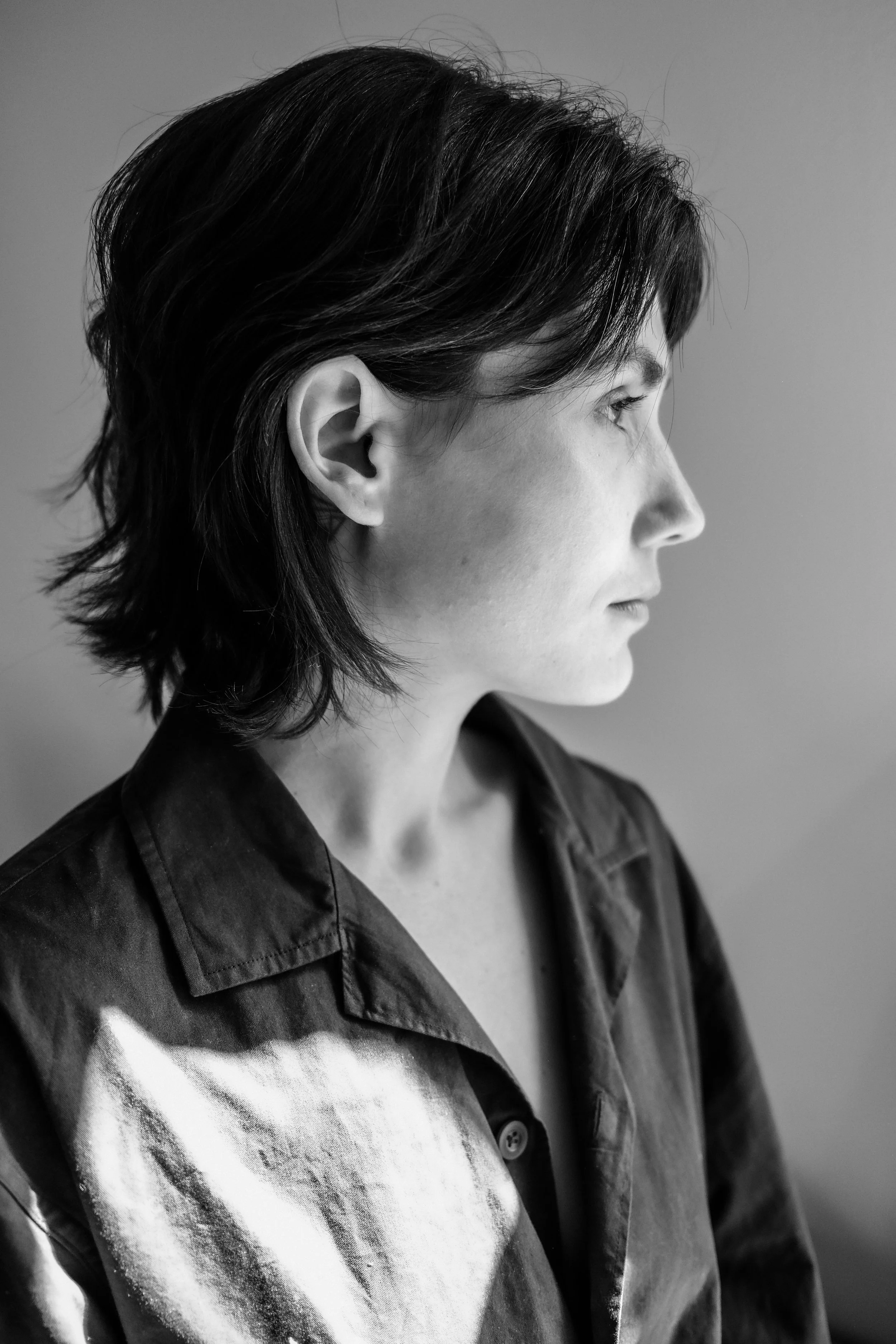 Portrait en noir et blanc d'une femme vue de profil, avec des cheveux courts et une expression sérieuse, portant une chemise en tissu foncé avec des motifs colorés.