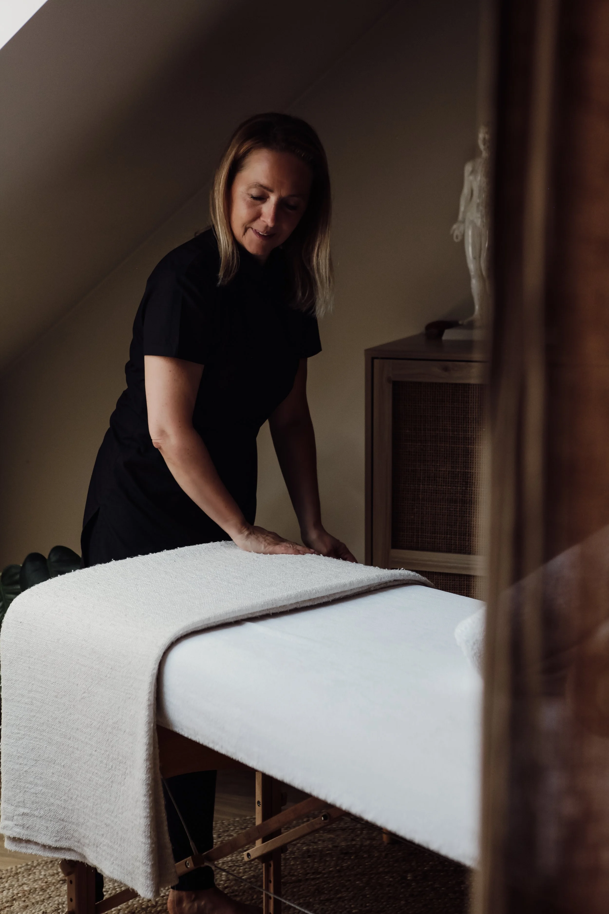 Une femme prépare un massage sur une table dans une pièce cosy.