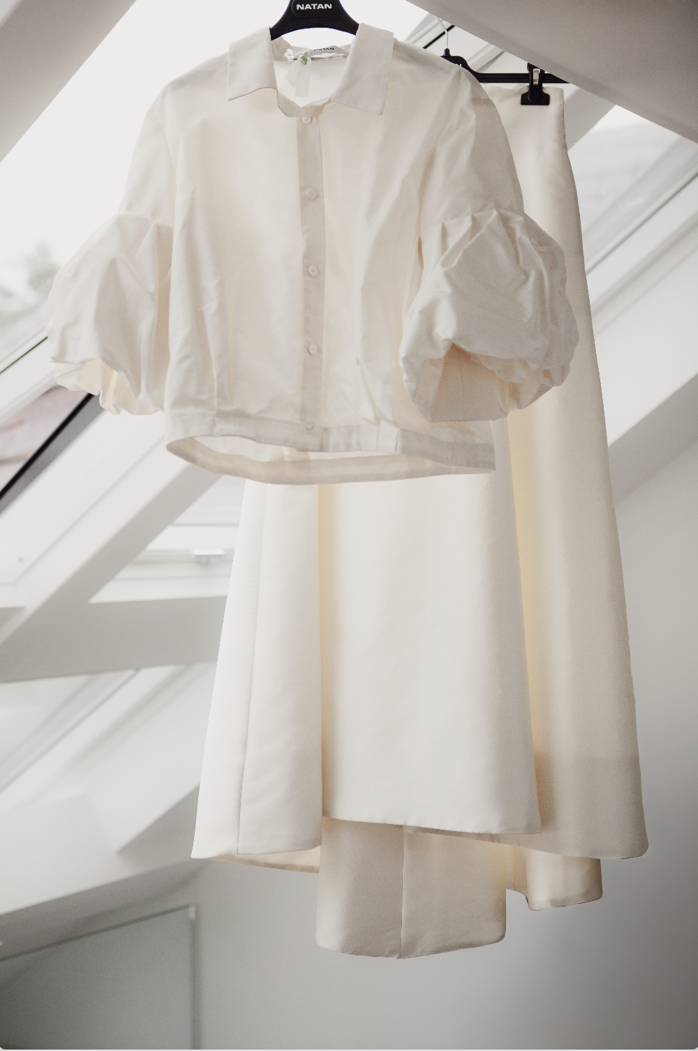 Chemisier blanc avec des manches bouffantes suspendu à un cintre sous un plafond en pente avec des fenêtres.