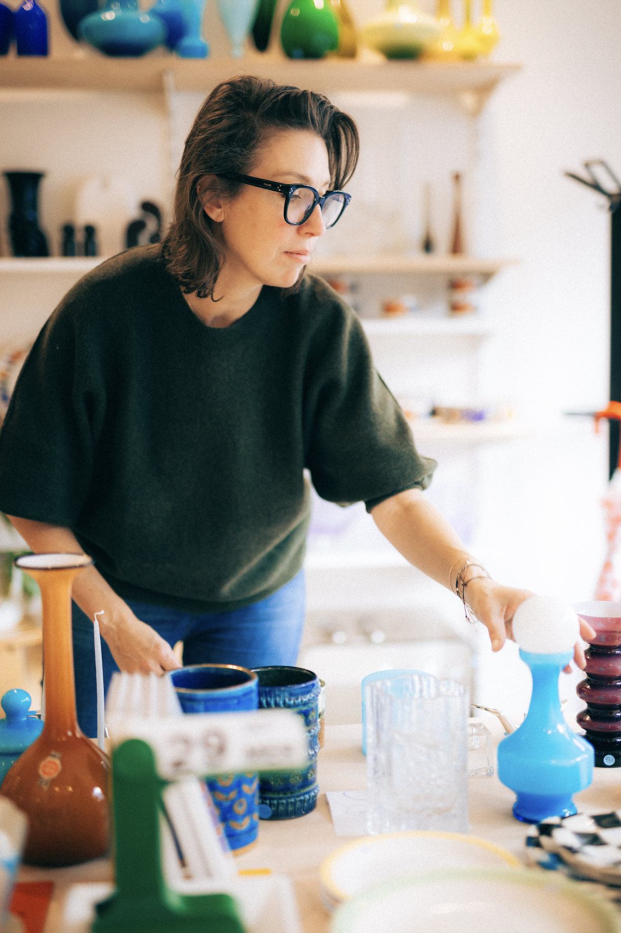 Une femme portant des lunettes noires regarde des objets en céramique colorés sur une table dans une boutique d'artisanat.