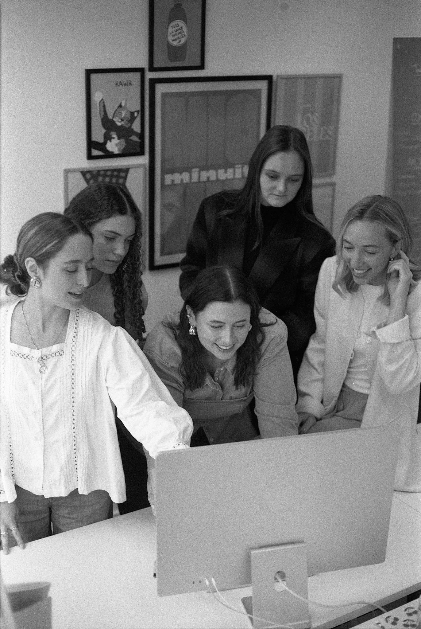 Cinq femmes regardent un écran d'ordinateur dans une pièce décorée avec plusieurs affiches murales.