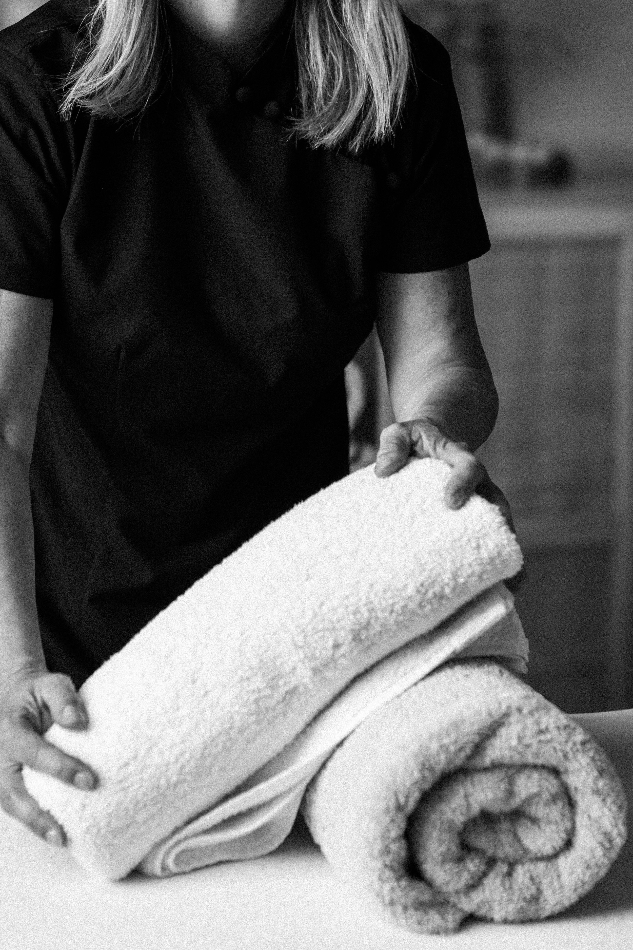 Une personne plie des serviettes de bain enroulées, vue de près en noir et blanc.