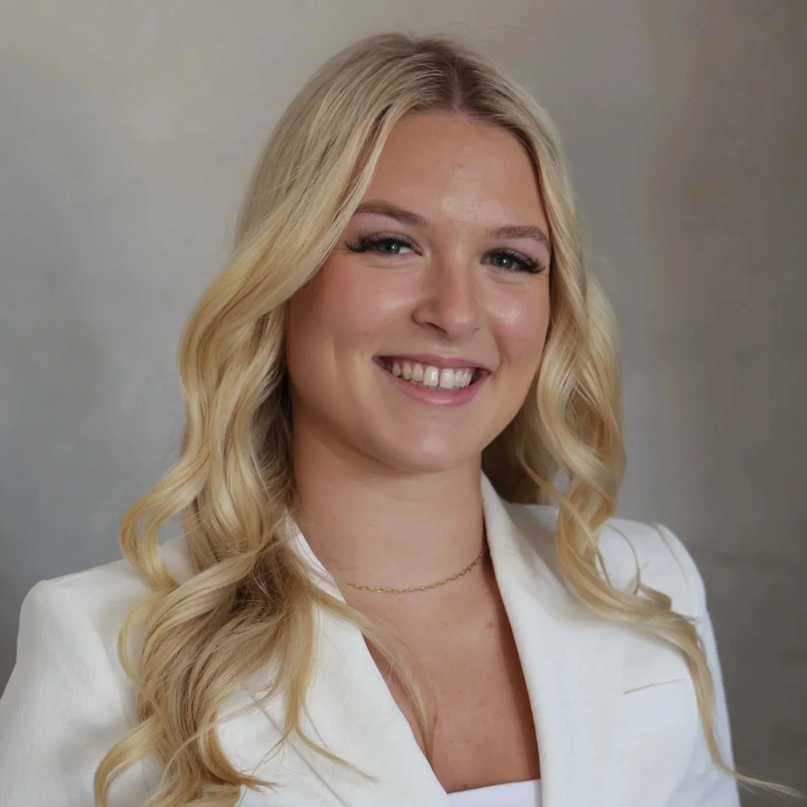 Smiling woman with long blonde hair wearing a white blazer.