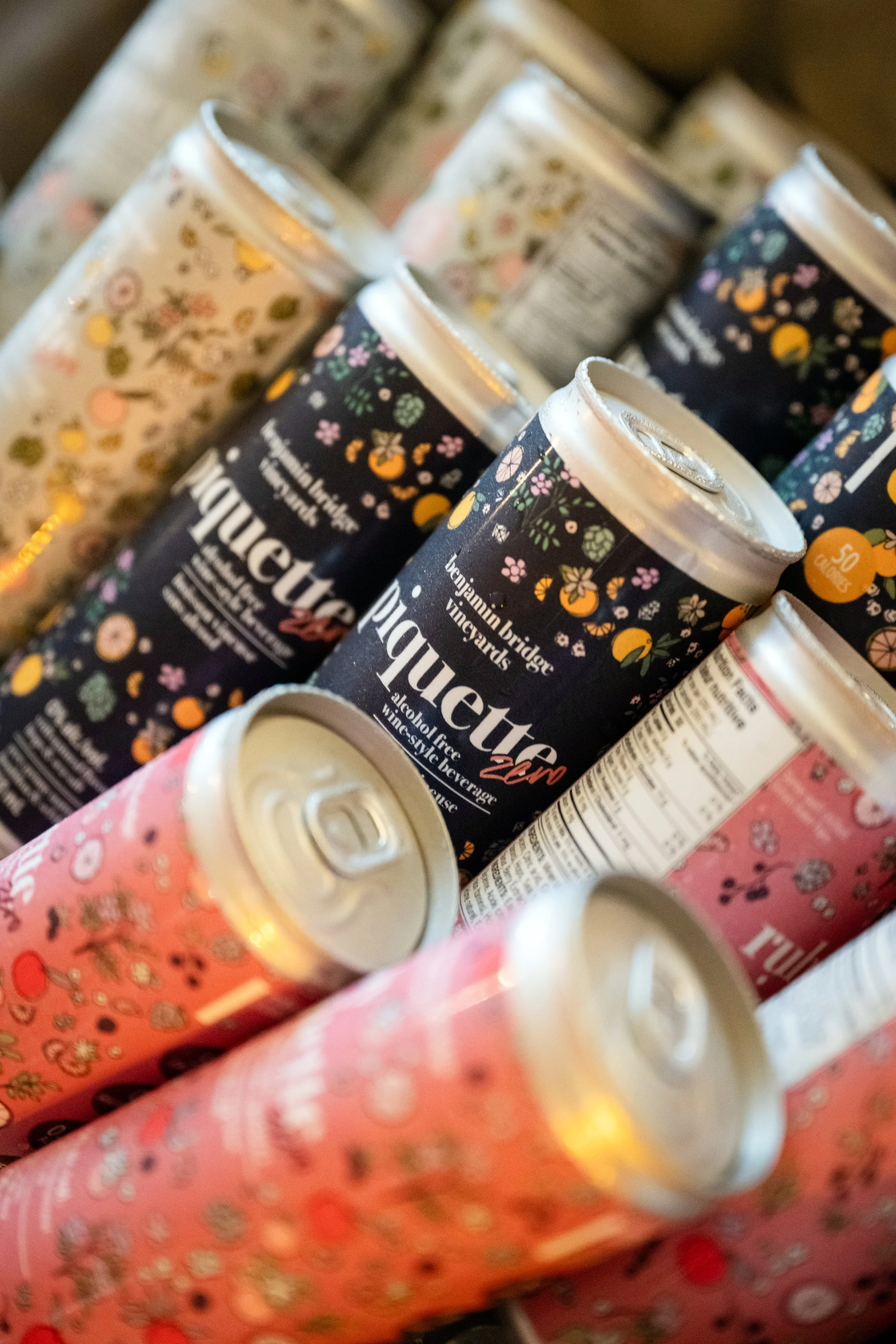 Close-up of cans of sparkling water with floral and colorful designs, including black, pink, and white patterns.