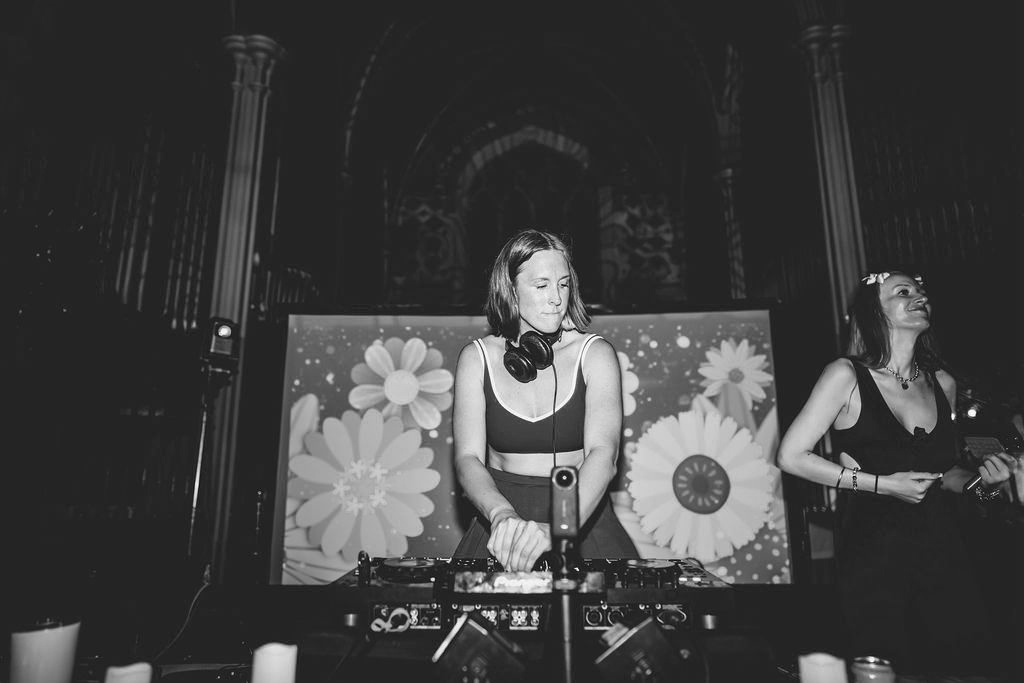 An image of a woman in front of a floral backdrop interacting with DJ equipment
