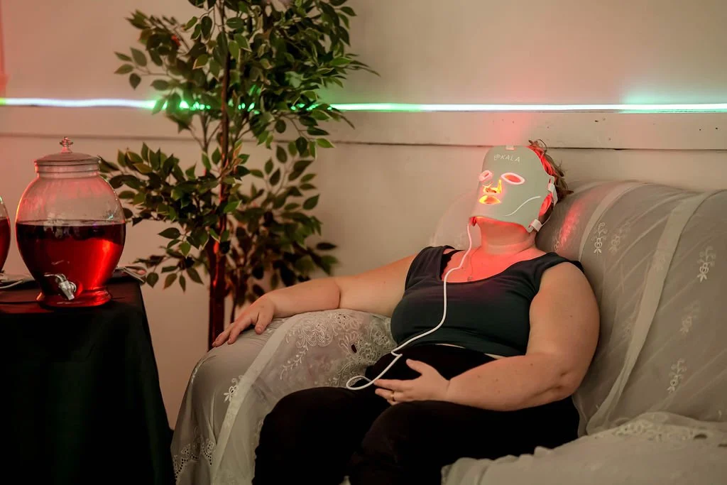 A woman sitting on a sofa with her eyes closed, wearing a face mask connected to a device, with a drink jar on a side table and a decorative potted plant nearby.