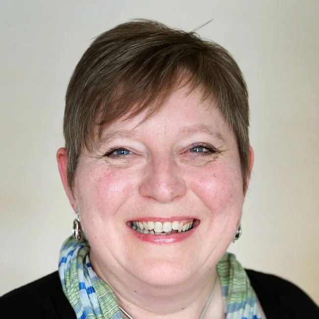 Close-up portrait of a woman with short brown hair, smiling, wearing earrings and a colorful scarf.